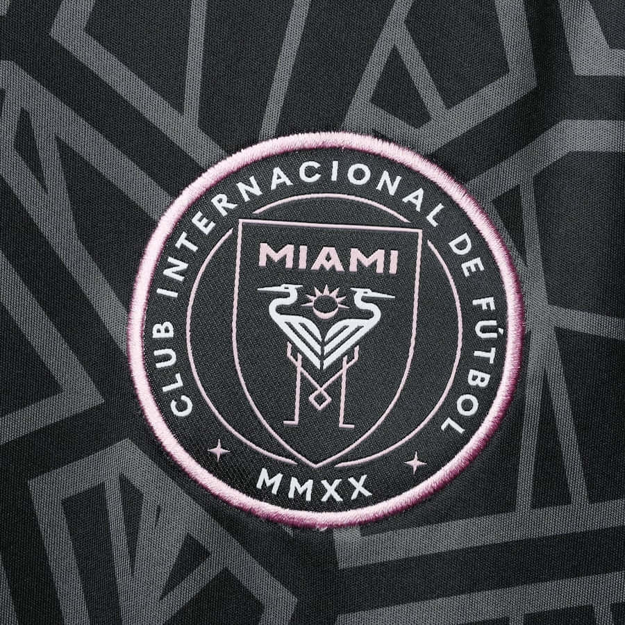 黑色美學 Inter Miami FC 官方隊徽標誌 壁紙 — 黑色布料上帶有幾何灰色圖案，粉紅色刺繡的邁阿密FC會徽特寫。