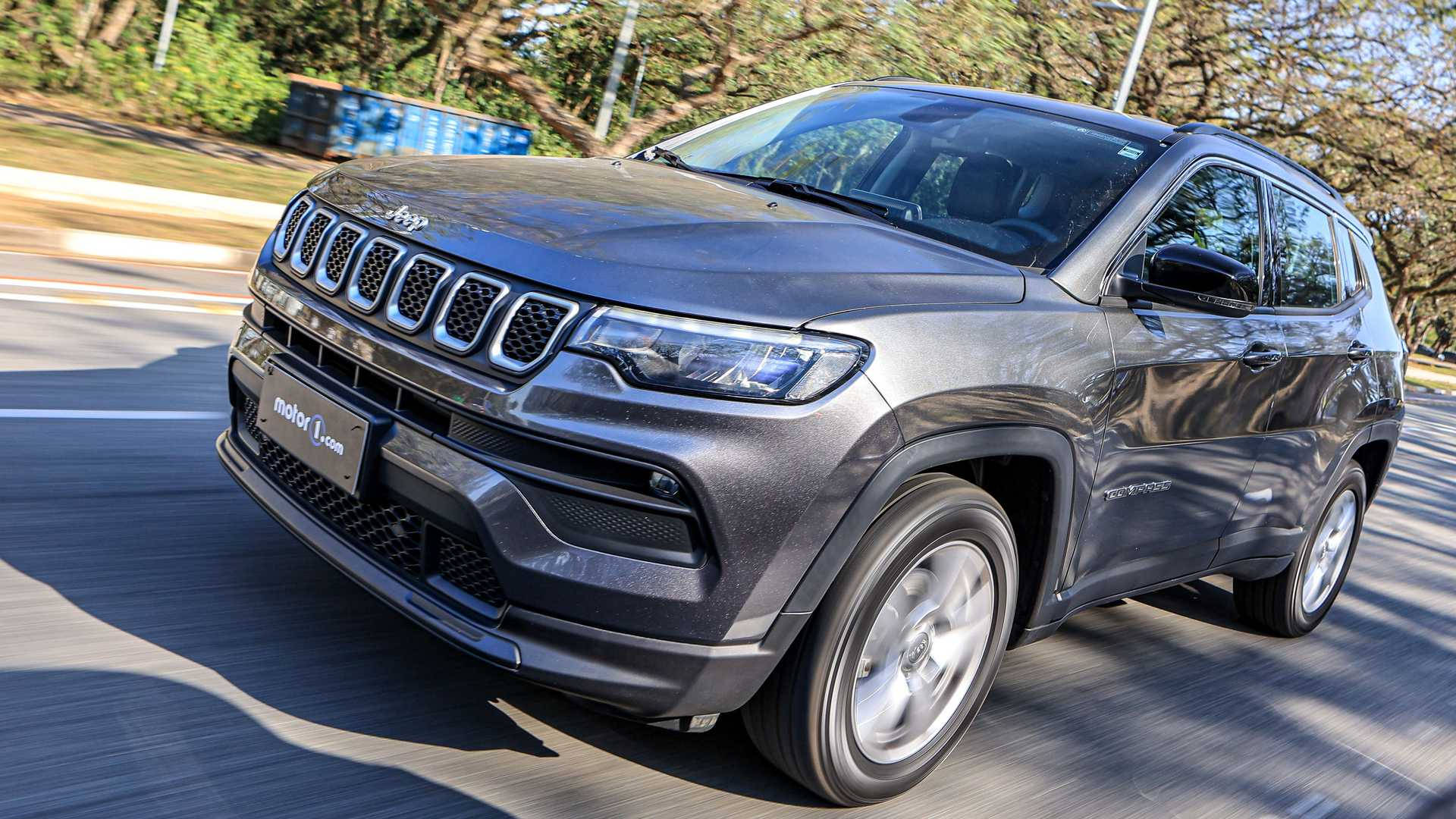 灰色Jeep Compass在陽光明媚的道路上行駛，有樹木和護欄。