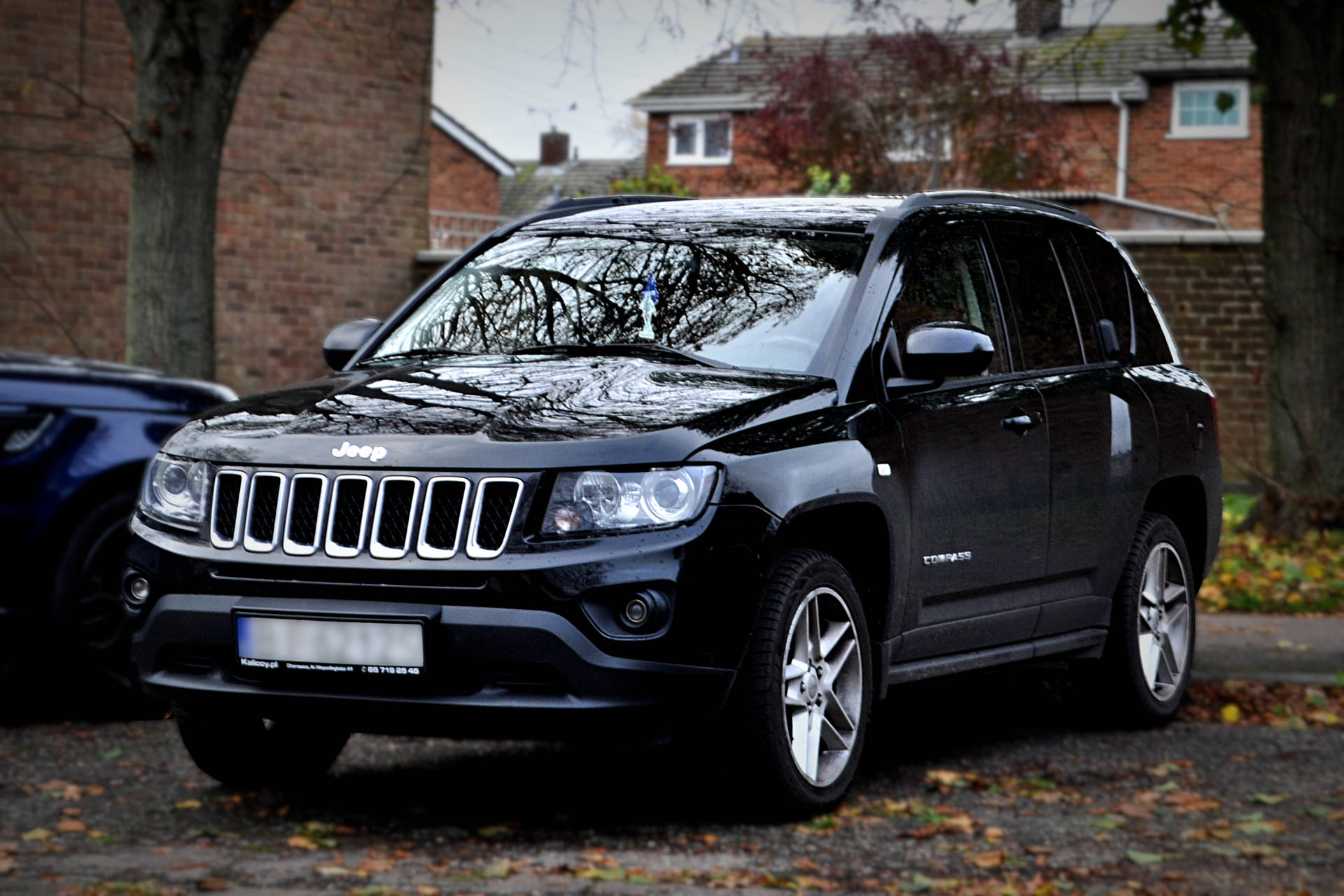 黑色Jeep Compass SUV停泊在鋪滿秋天落葉的車道上。