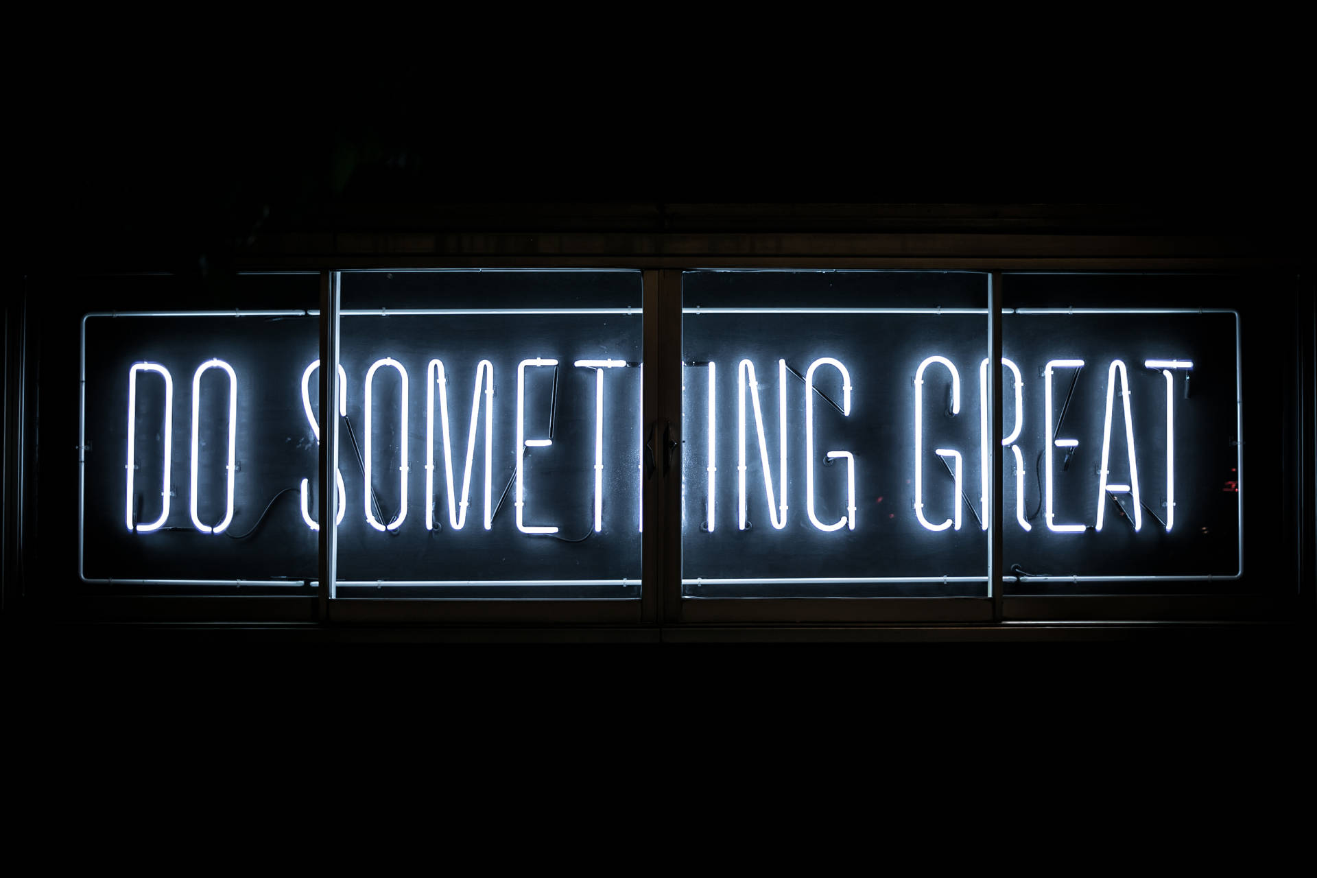 一個明亮的白色霓虹燈牌，上面寫著「Do Something Great」，在黑暗的窗戶中。 — 酷 壁紙