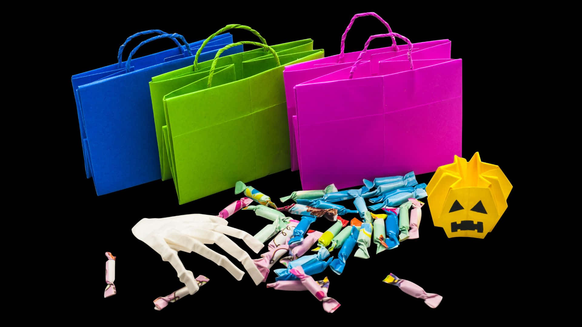 Trick Or Treat Bags 桌布 壁紙 — 黑色背景上，散落著充滿活力的萬聖節袋子和糖果，配以白色骷髏手和黃色南瓜燈。