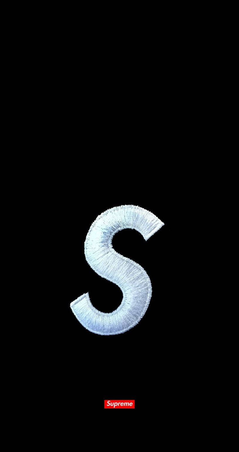 黑色背景上的Supreme標誌 壁紙 — 一個大型紋理銀色刺繡字母S居中於黑色背景上，底部有一個細小的紅色Supreme標誌。