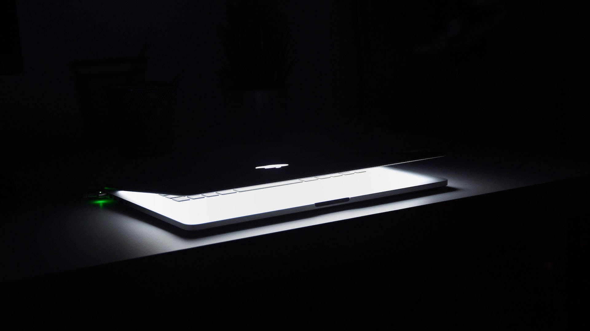 在黑暗的桌子上帶有綠色電源指示燈的發光筆記型電腦。