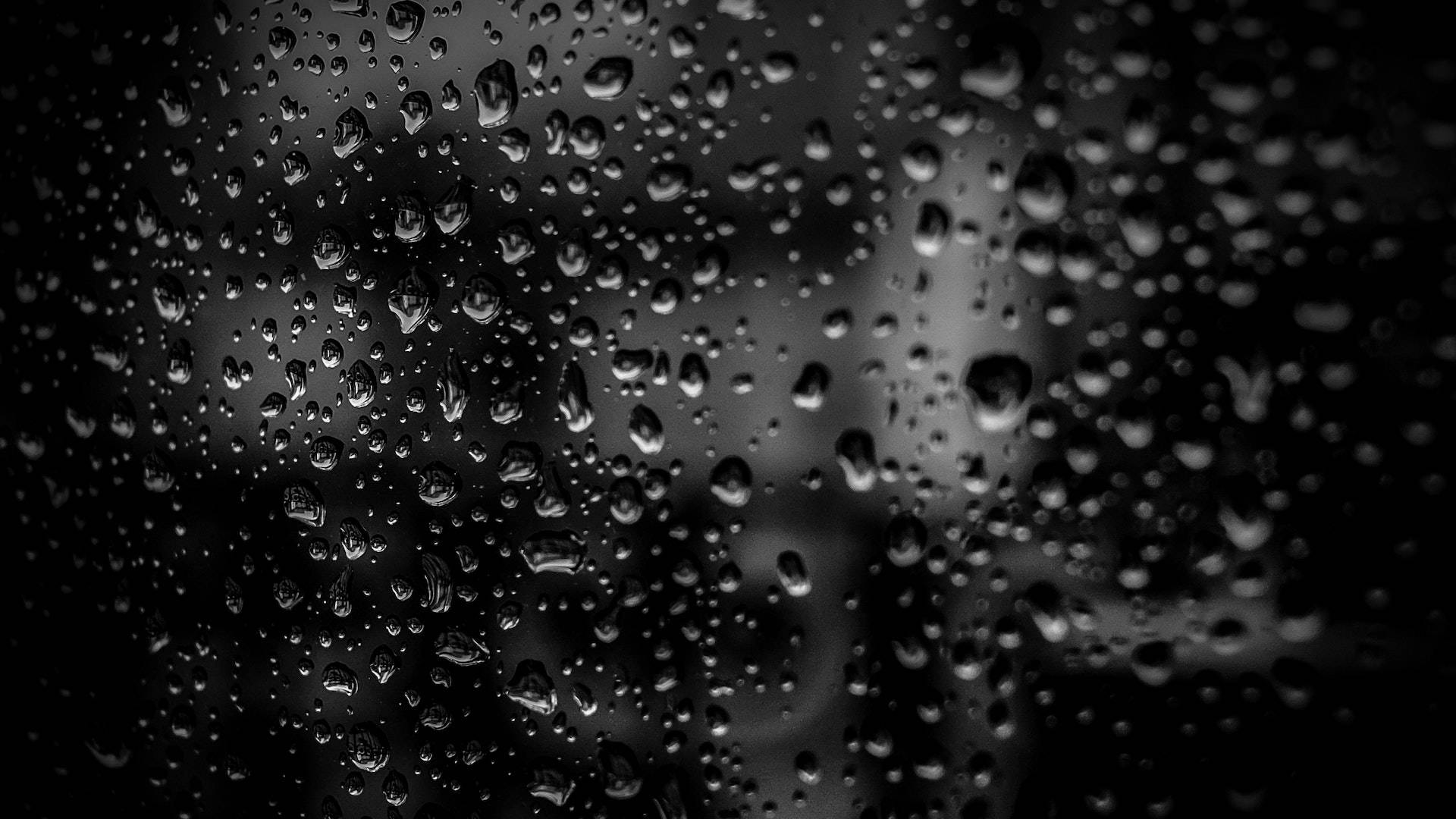 玻璃上的雨滴遮擋了模糊的灰階城市景觀。