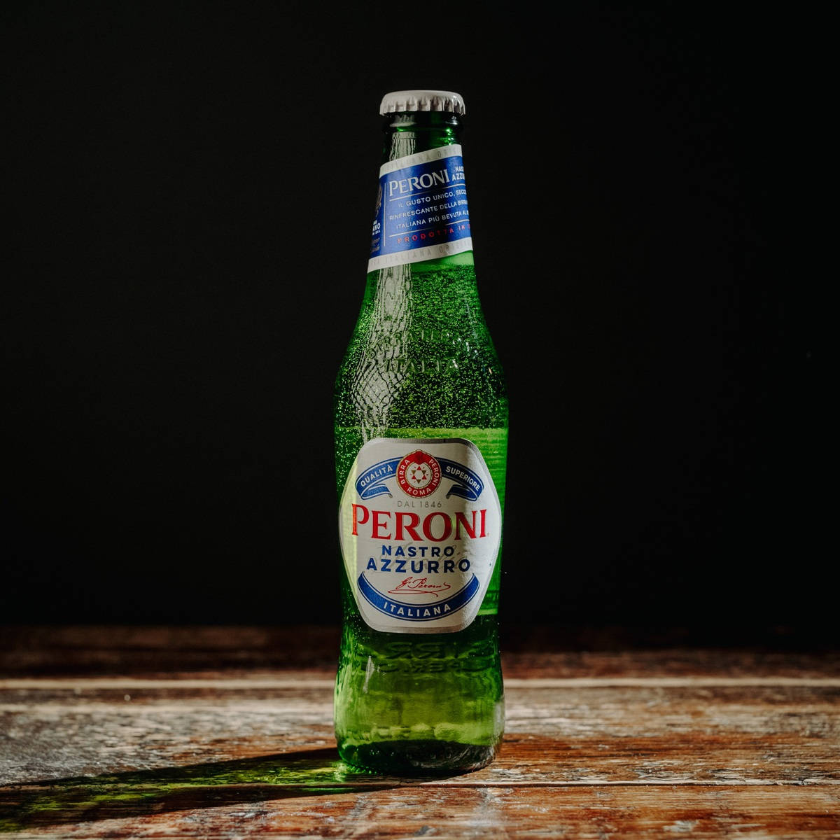 深色背景的木桌上放著冰凍的 Peroni 啤酒瓶。