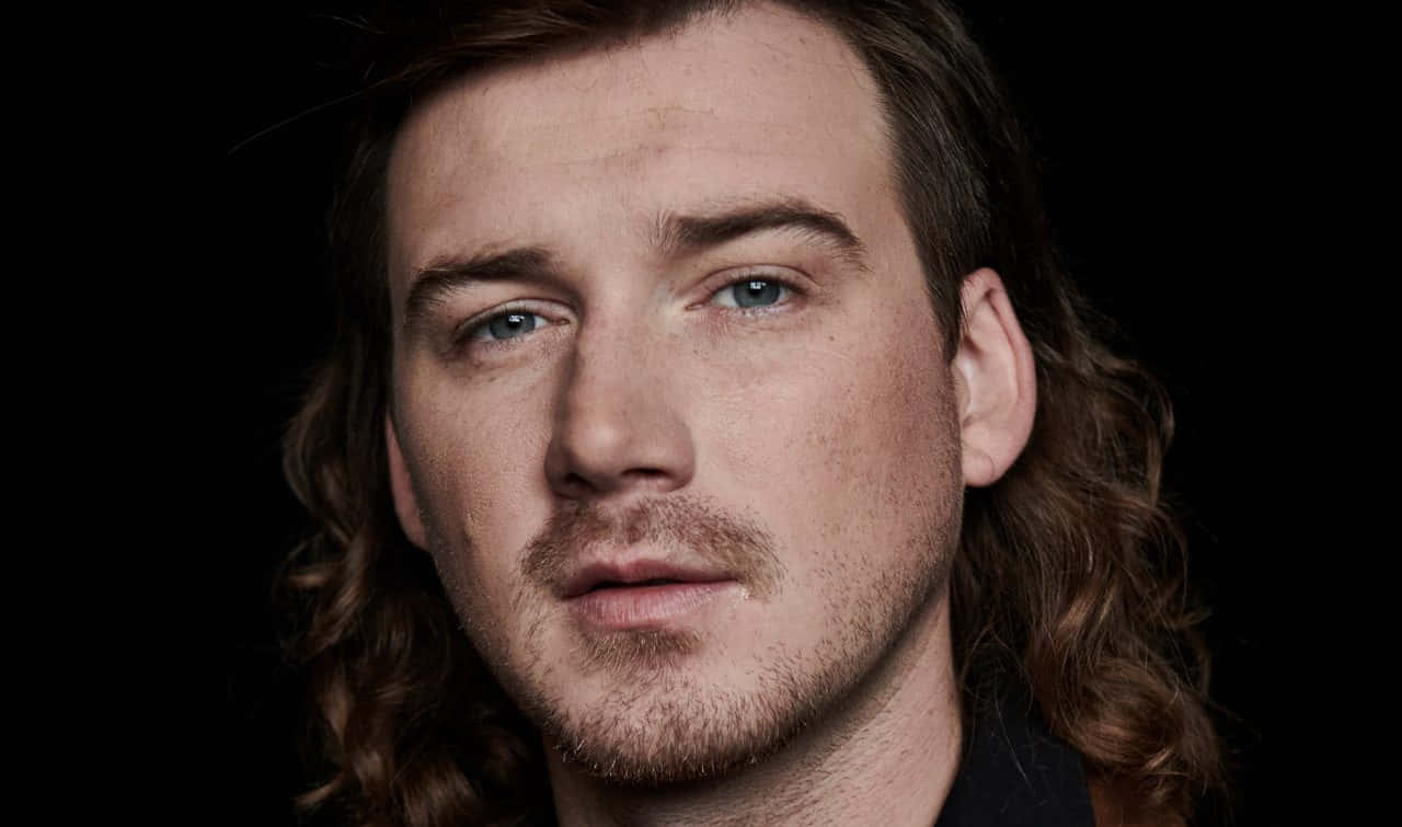 Morgan Wallen 桌布 壁紙 — 黑色背景前，長棕色頭髮和藍眼睛男子的特寫肖像。