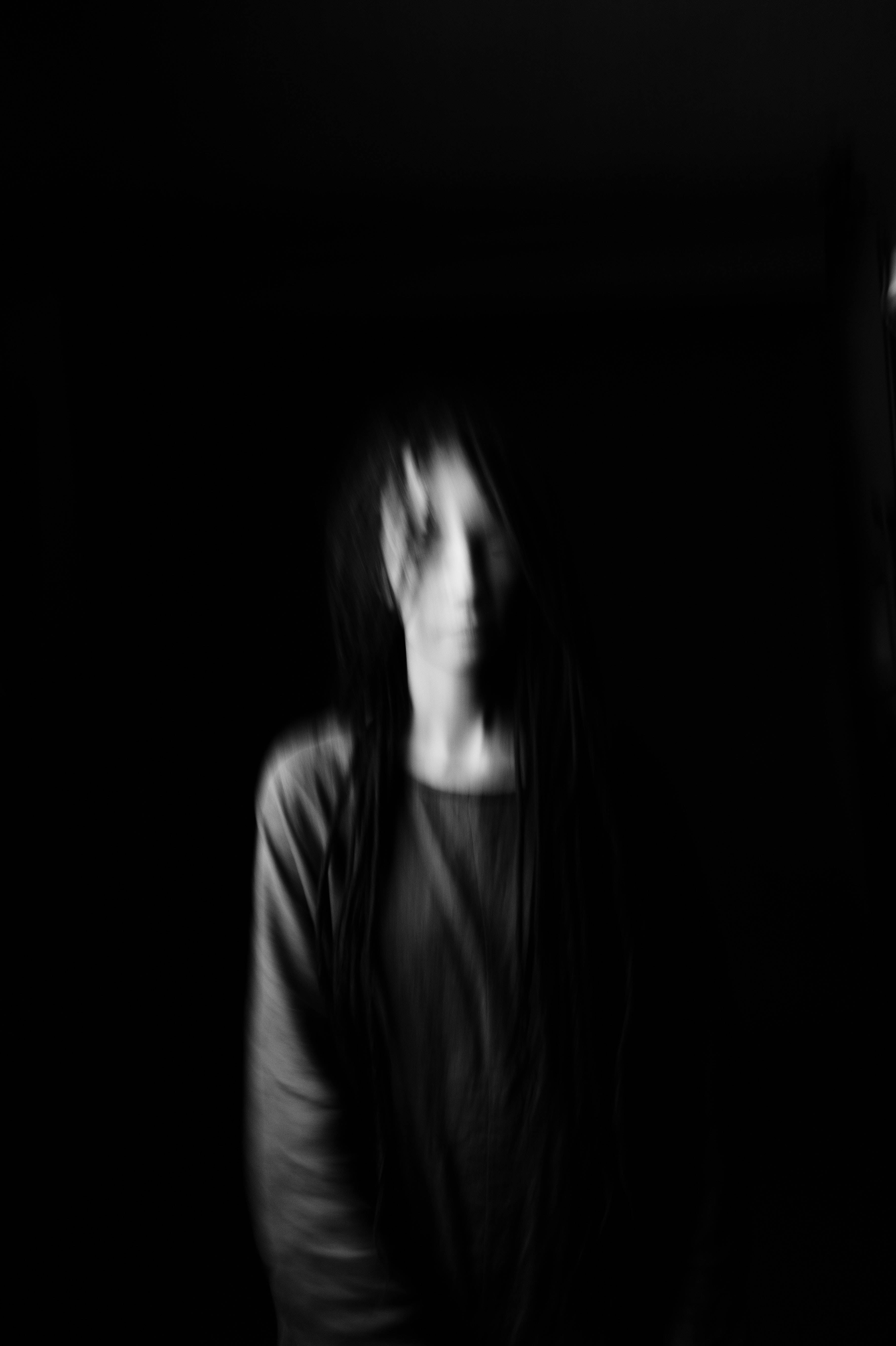 黑色背景模糊女子 壁紙 — 一個模糊的單色長髮人物站在近乎黑暗的環境中，營造出令人毛骨悚然且神秘的氛圍。