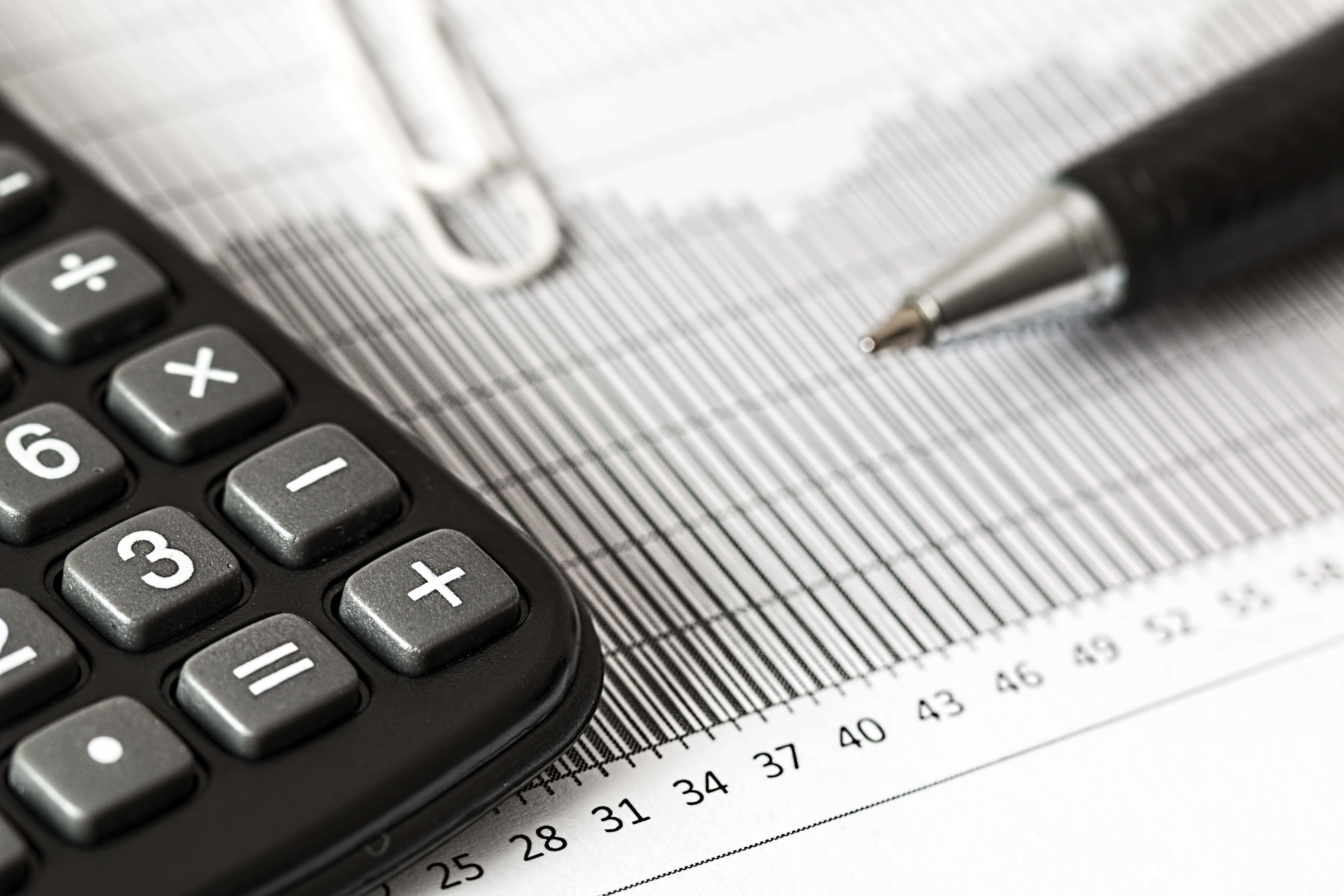 Calculator 桌布 壁紙 — 黑色計算機、筆和間尺的特寫，放在帶有財務數據的圖表紙上。