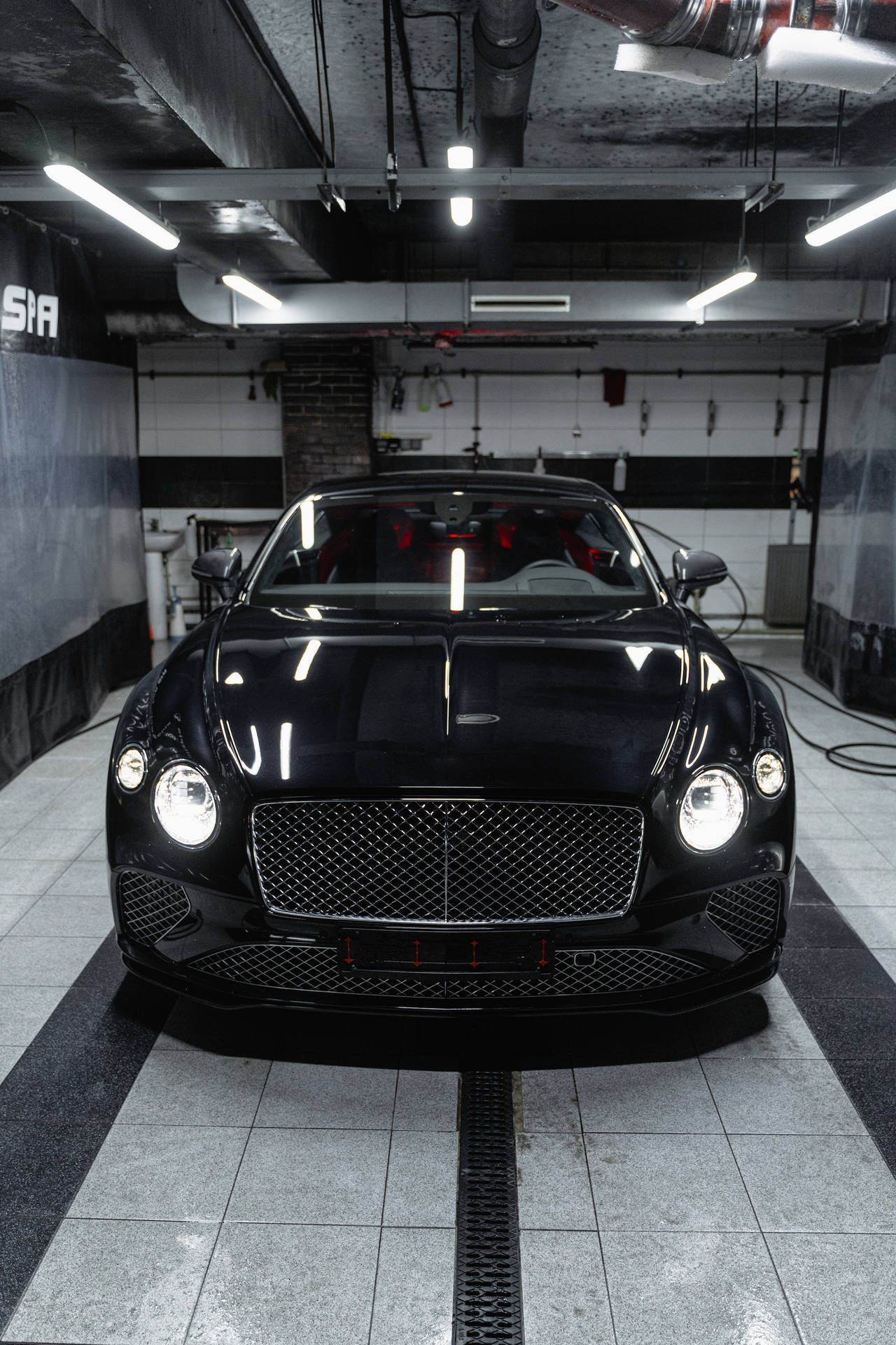 光線充足的工業車庫中，瓷磚地板上的黑色賓利 Continental GT。