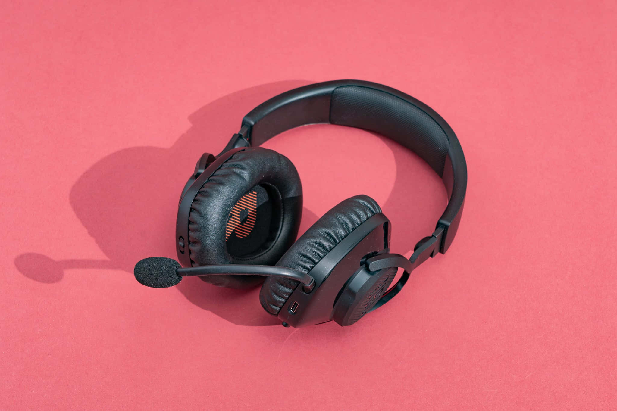 Gaming Headsets 桌布 壁紙 — 黑色遊戲耳機連咪高峰放在純珊瑚粉紅色背景上，投射出柔和陰影。
