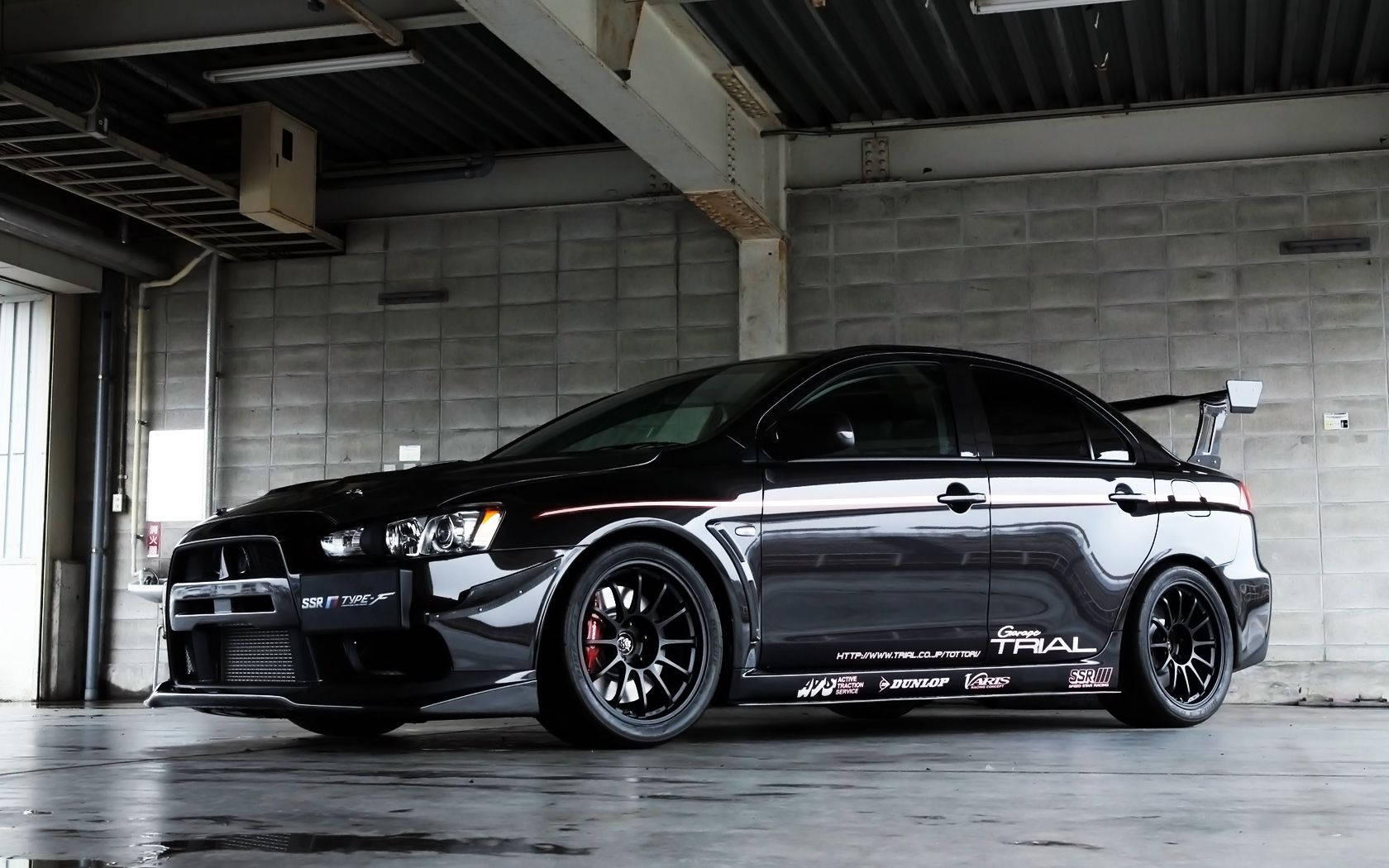 黑色三菱Lancer Evolution拉力賽車在混凝土車庫內，帶有贊助商貼紙。