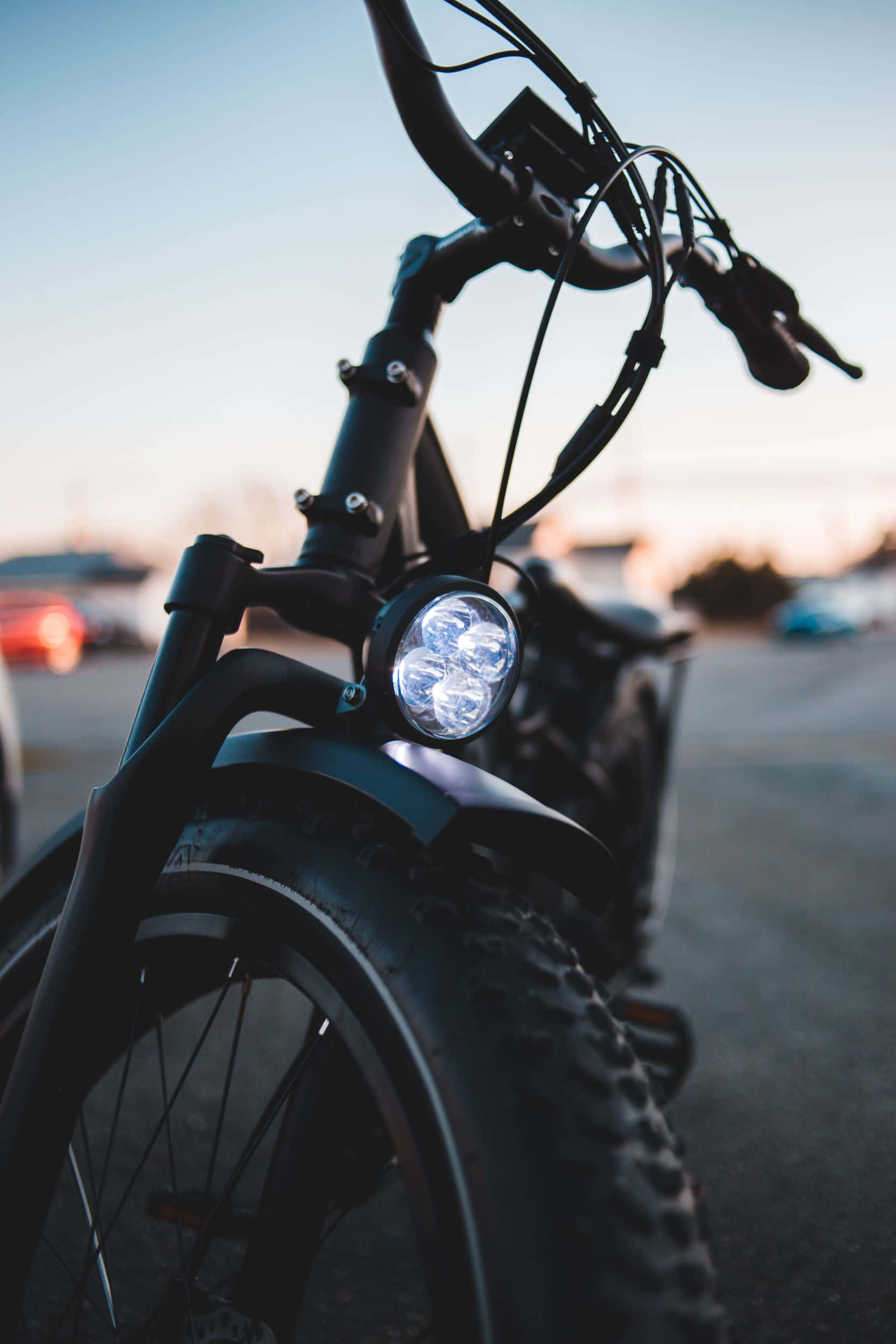 Electric Bike 桌布 壁紙 — 黑色電動單車的手把和明亮頭燈在柔和日落天空下的特寫。