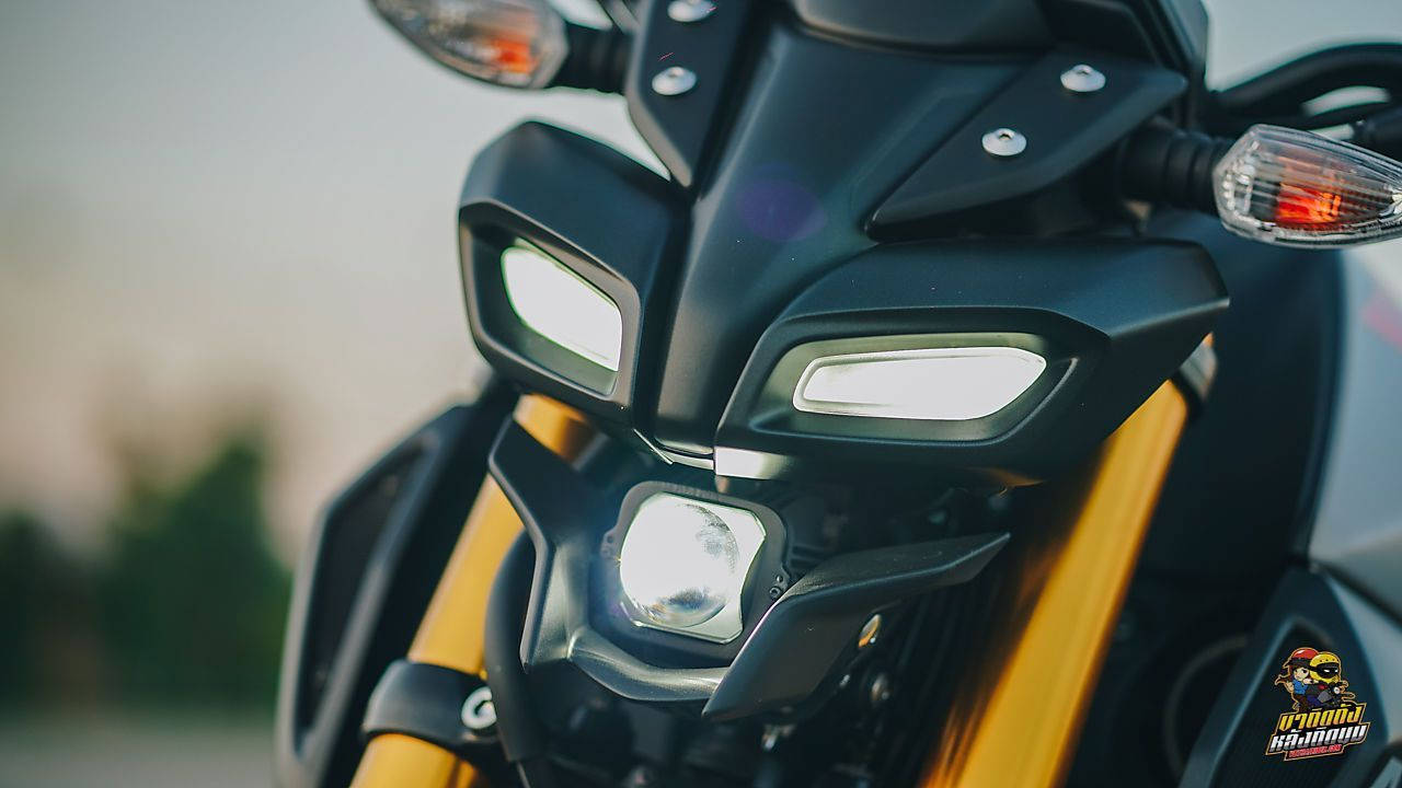 yamaha mt 15 桌布 壁紙 — 黑色電單車發光頭燈和琥珀色前叉的微距特寫，背景柔和模糊。