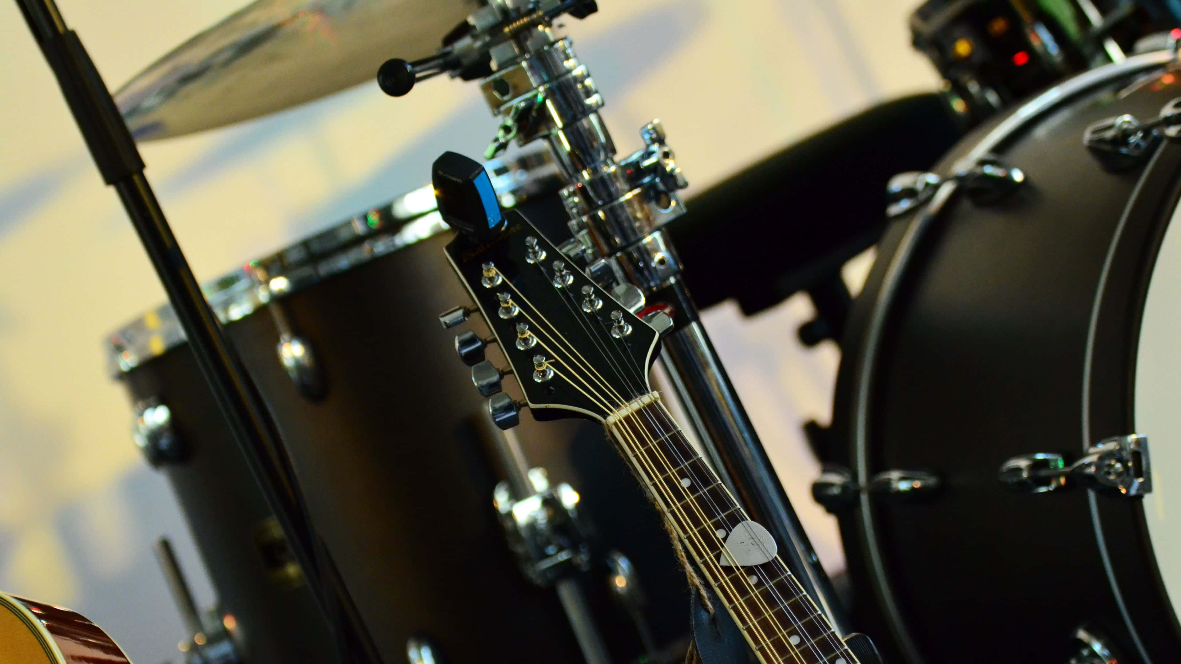 Musical 桌布 壁紙 — 黑色電結他琴頭近距離特寫，旁邊係一套帶有閃亮鉻金屬件同黑色鼓嘅鼓組。