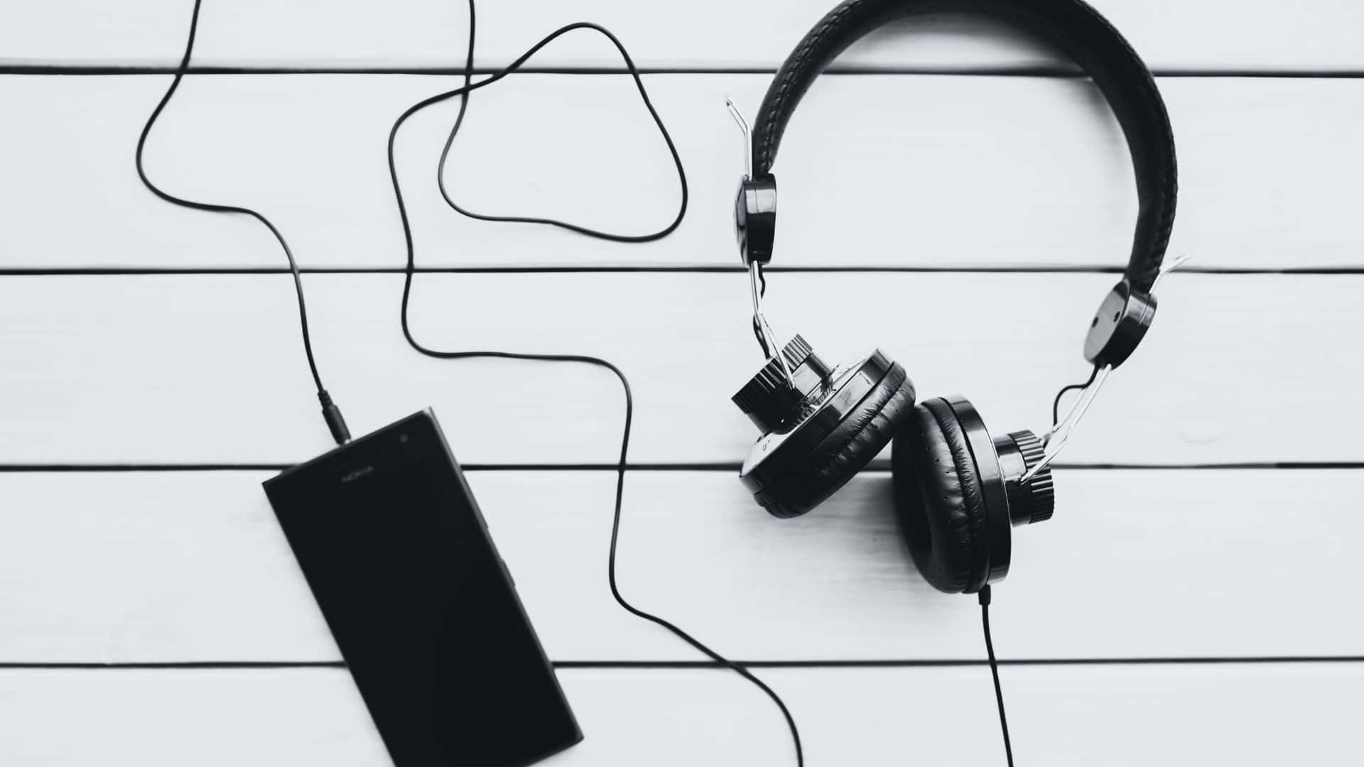 Black And White Music 桌布 壁紙 — 黑色頭戴式耳機和智能手機以單色調放在白色木板上。