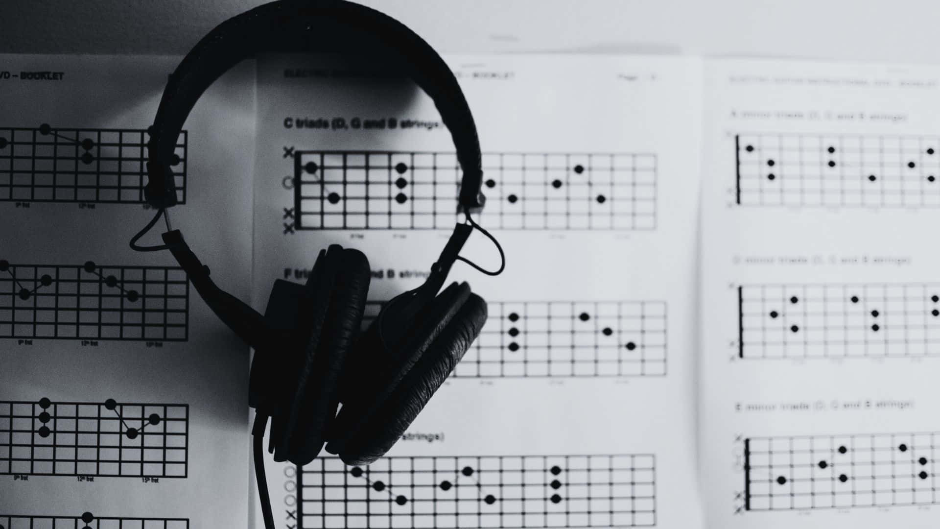 Black And White Music 桌布 壁紙 — 黑色頭戴式耳機放在單色構圖的結他和弦圖譜上。