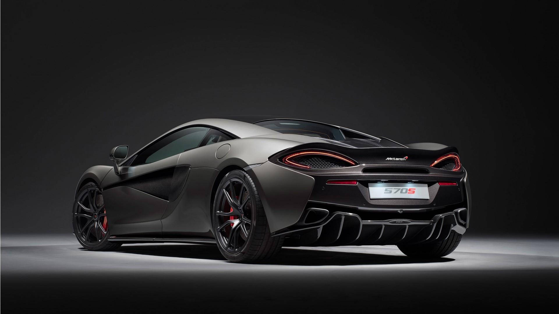黑色麥拉倫 570s 壁紙 — 一輛時尚的啞光灰色McLaren 570S跑車，帶有發光的紅色尾燈，在黑暗背景下的戲劇性工作室聚光燈中展示。