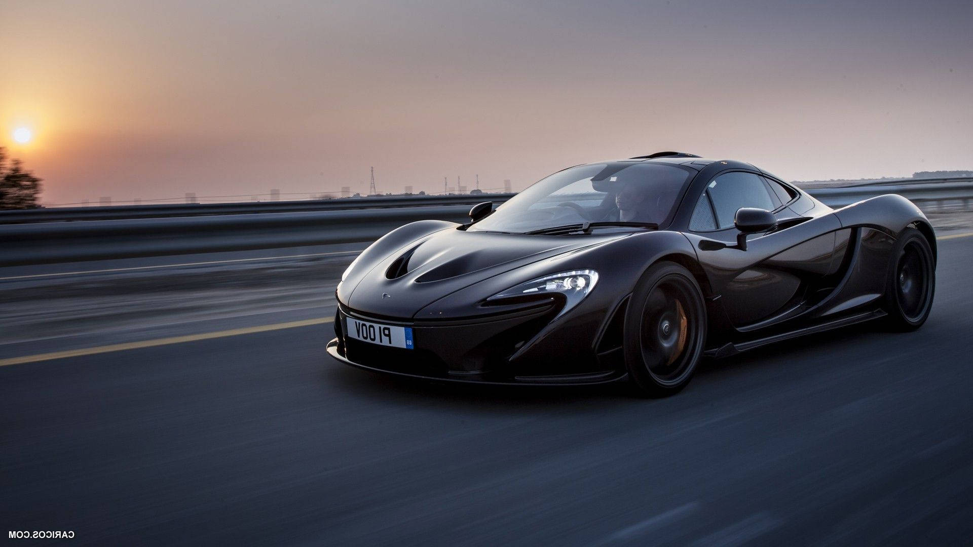 黑色麥拉倫 P1 超跑 壁紙 — 一架流線型黑色McLaren P1在日落時分沿高速公路飛馳，帶有動態模糊和溫暖的金色光線。