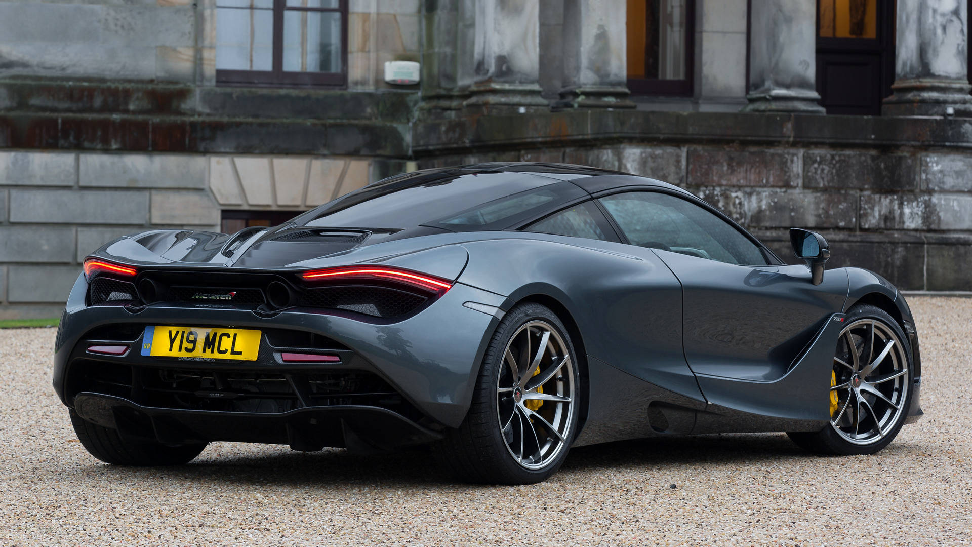 黑色麥拉倫720S 4K 壁紙 — 一架時尚的啞光灰色McLaren 720S跑車停泊在宏偉石建築前的碎石上。
