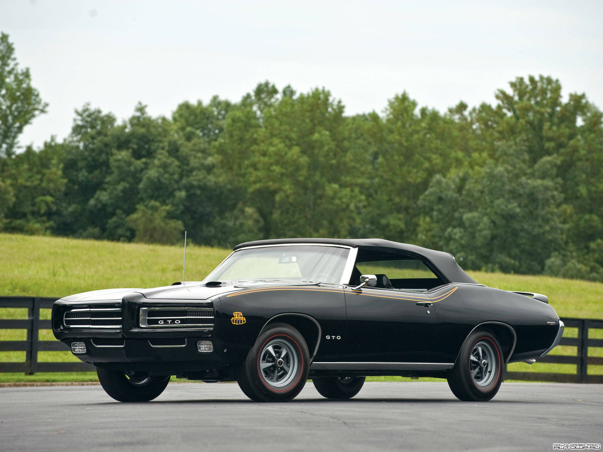 黑色龐蒂克GTO汽車 壁紙 — 一架時尚黑色經典Pontiac GTO開篷車停泊在瀝青路上，背景有綠樹和草地。