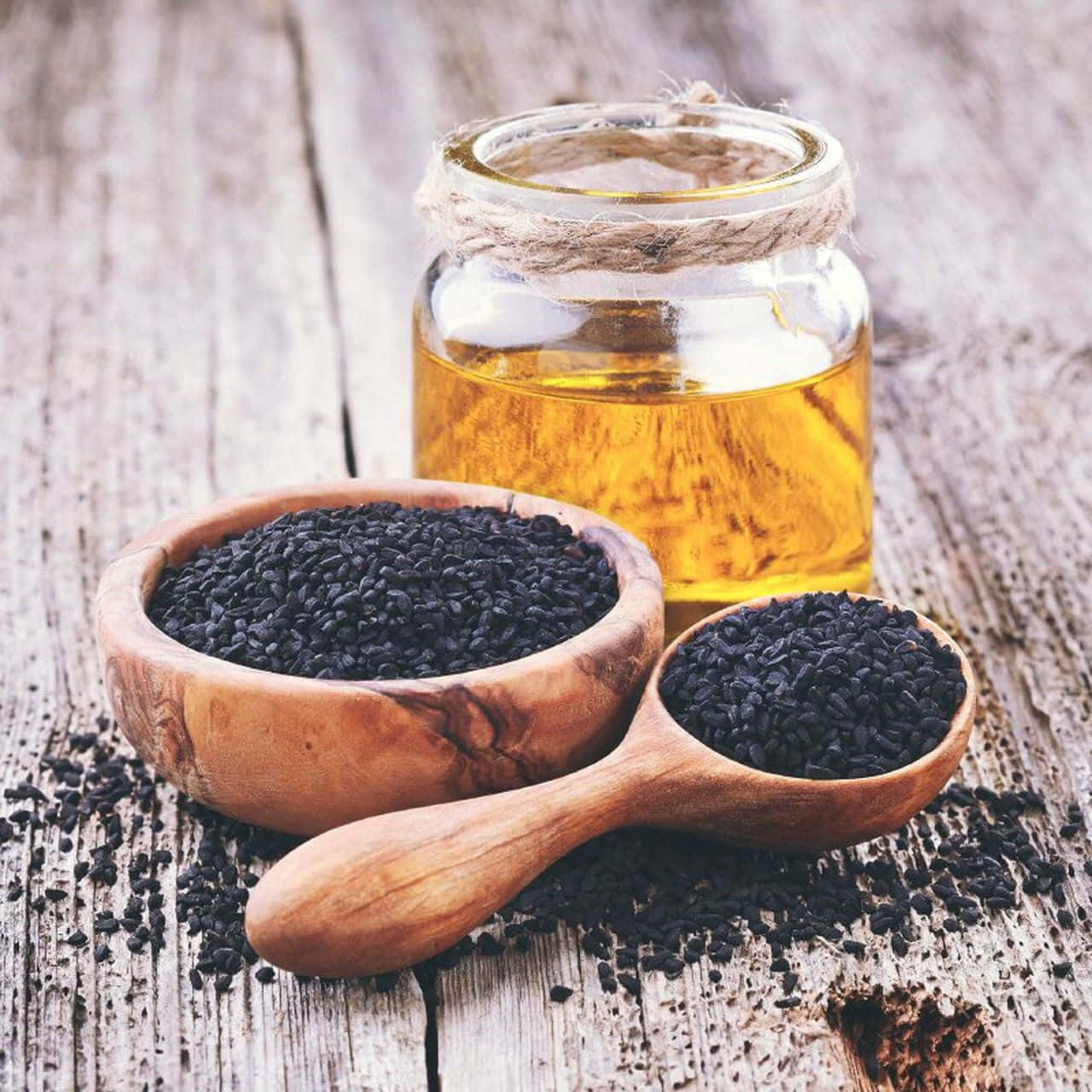 Black Cumin 桌布 壁紙 — 黑芝麻從木碗和湯匙中灑出，旁邊放著一瓶金黃色的芝麻油在風化的木質表面上。