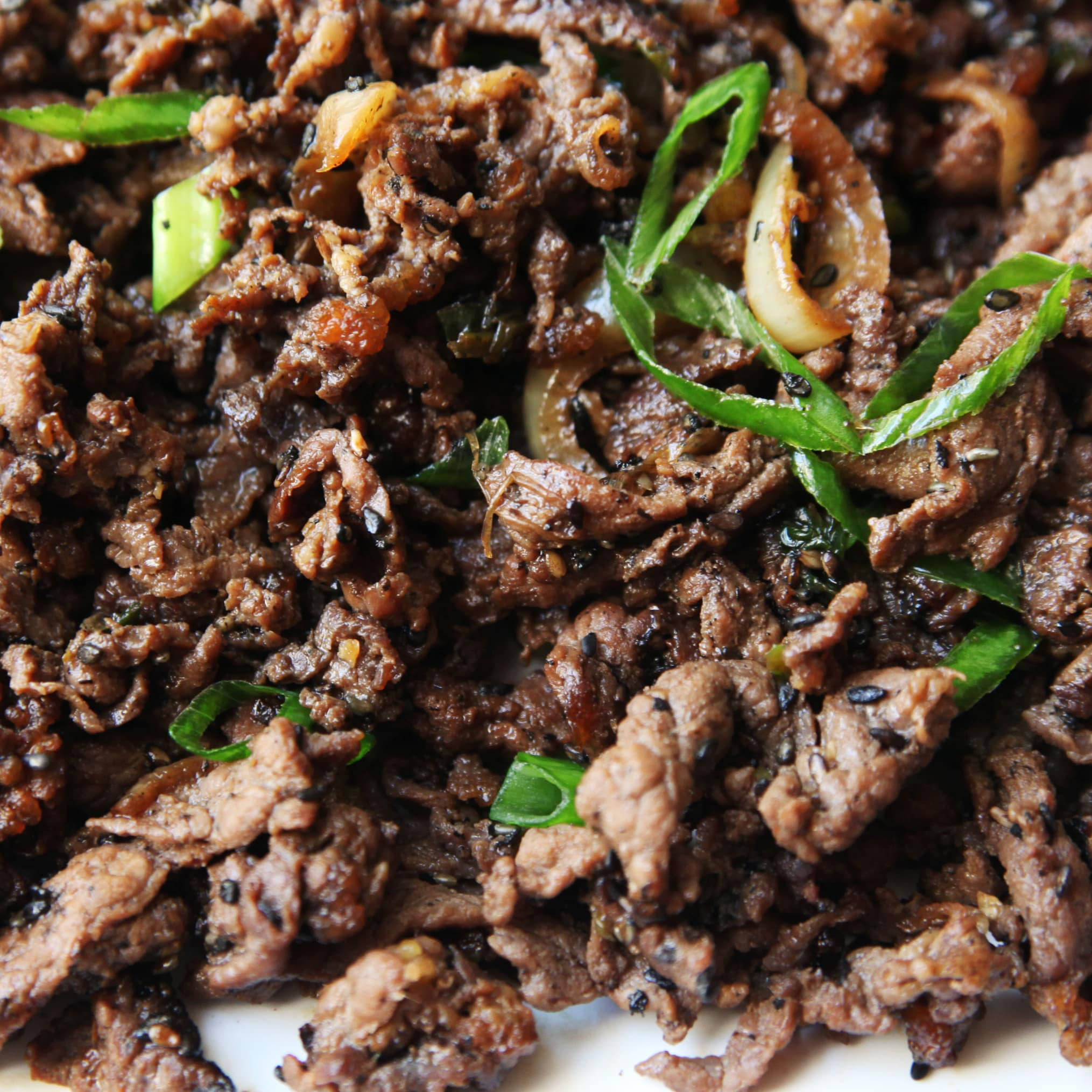 黑芝麻韓式牛肉 壁紙 — 特寫鏡頭：惹味嘅炒牛肉條，配上青蔥、芝麻同焦糖洋蔥，醬汁閃閃發光。