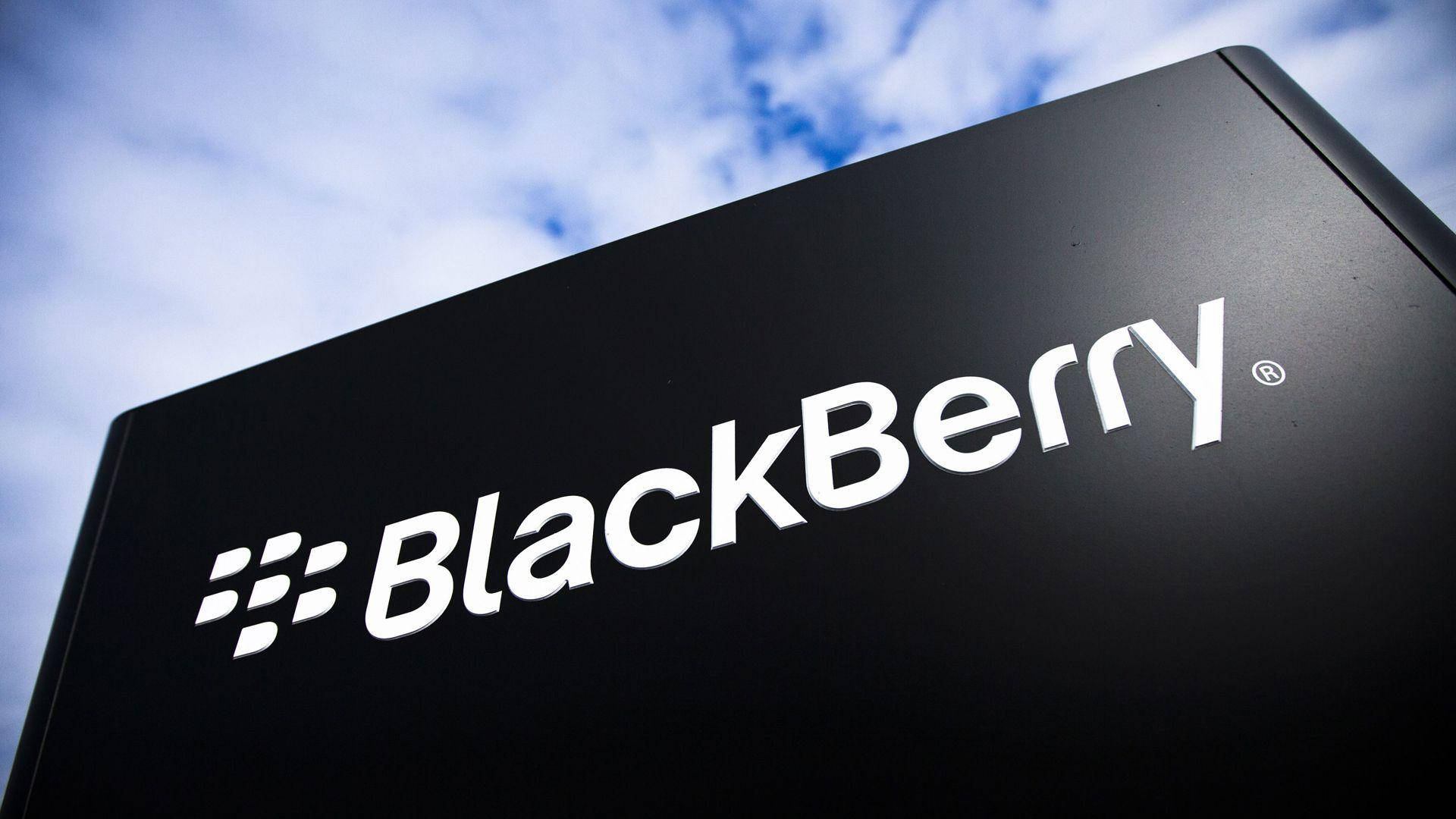 黑莓霧面黑 壁紙 — 一個時尚的黑色BlackBerry標誌牌，帶有白色標誌，矗立在晴朗的藍天和白雲之間。