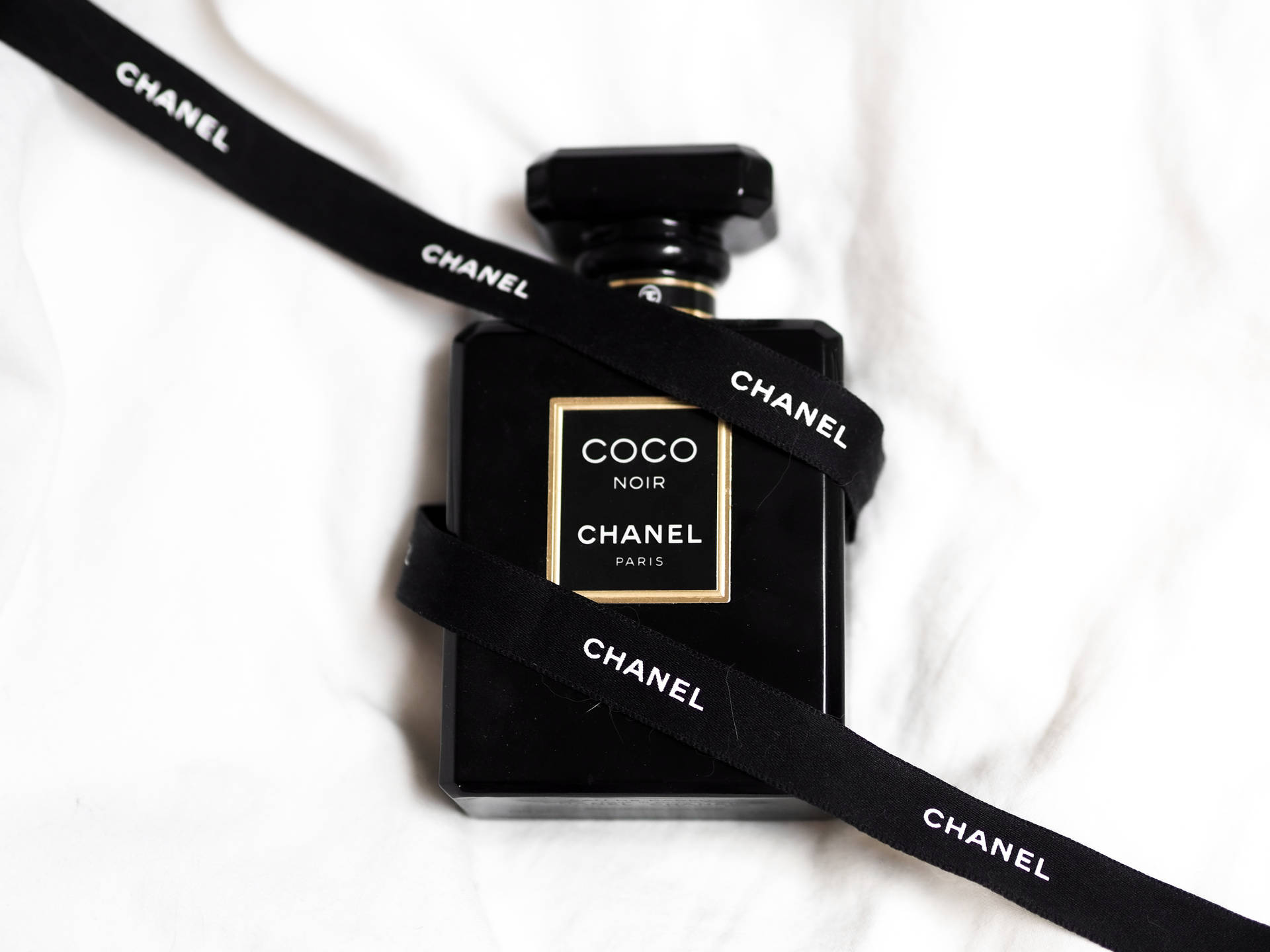 黑色 Chanel Coco Noir 香水瓶包裹黑色絲帶放在白色布料上。