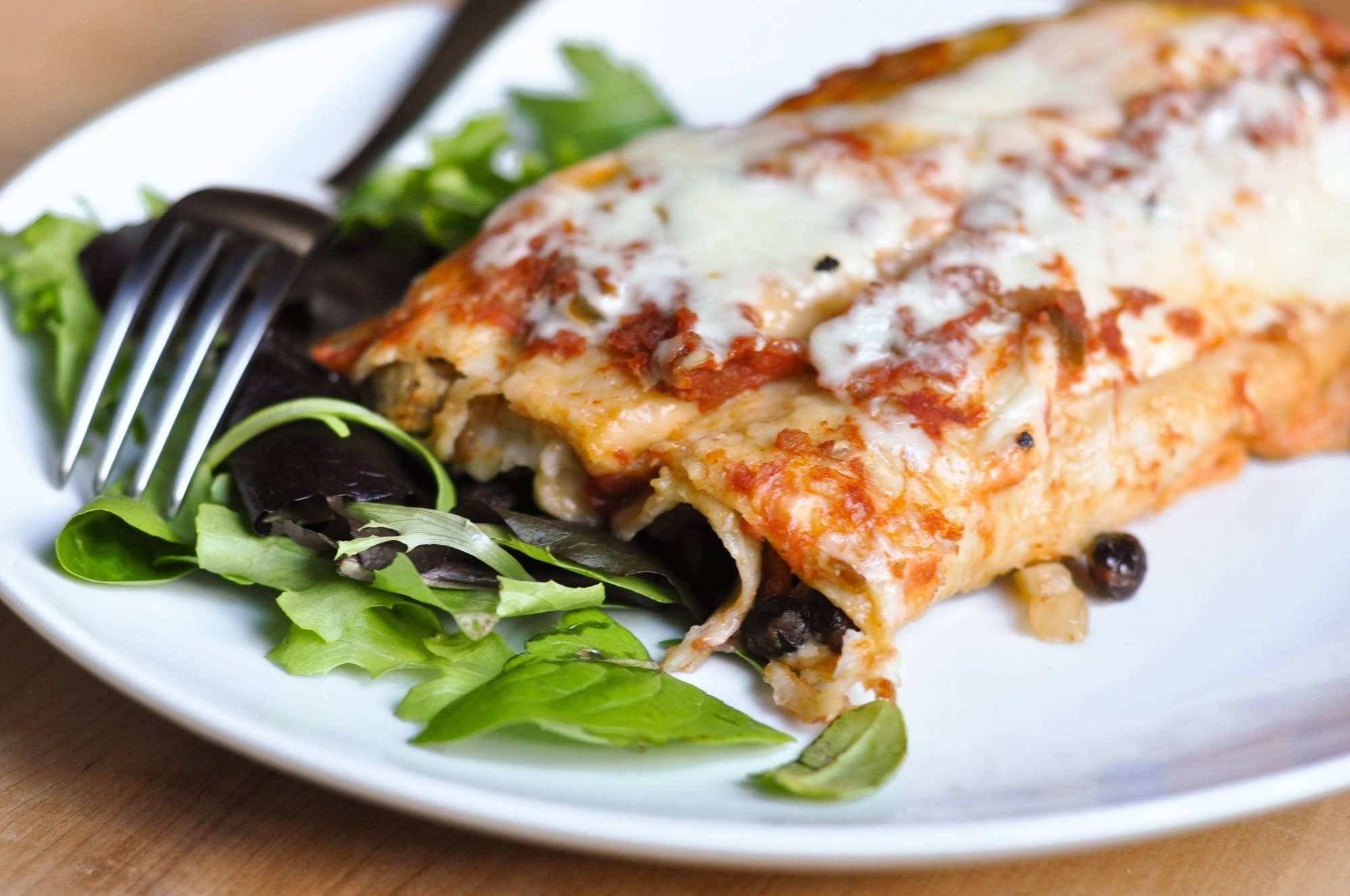 黑豆 enchiladas 盤 壁紙 — 一個芝士焗玉米卷配黑豆和新鮮蔬菜放在白色碟上的特寫。