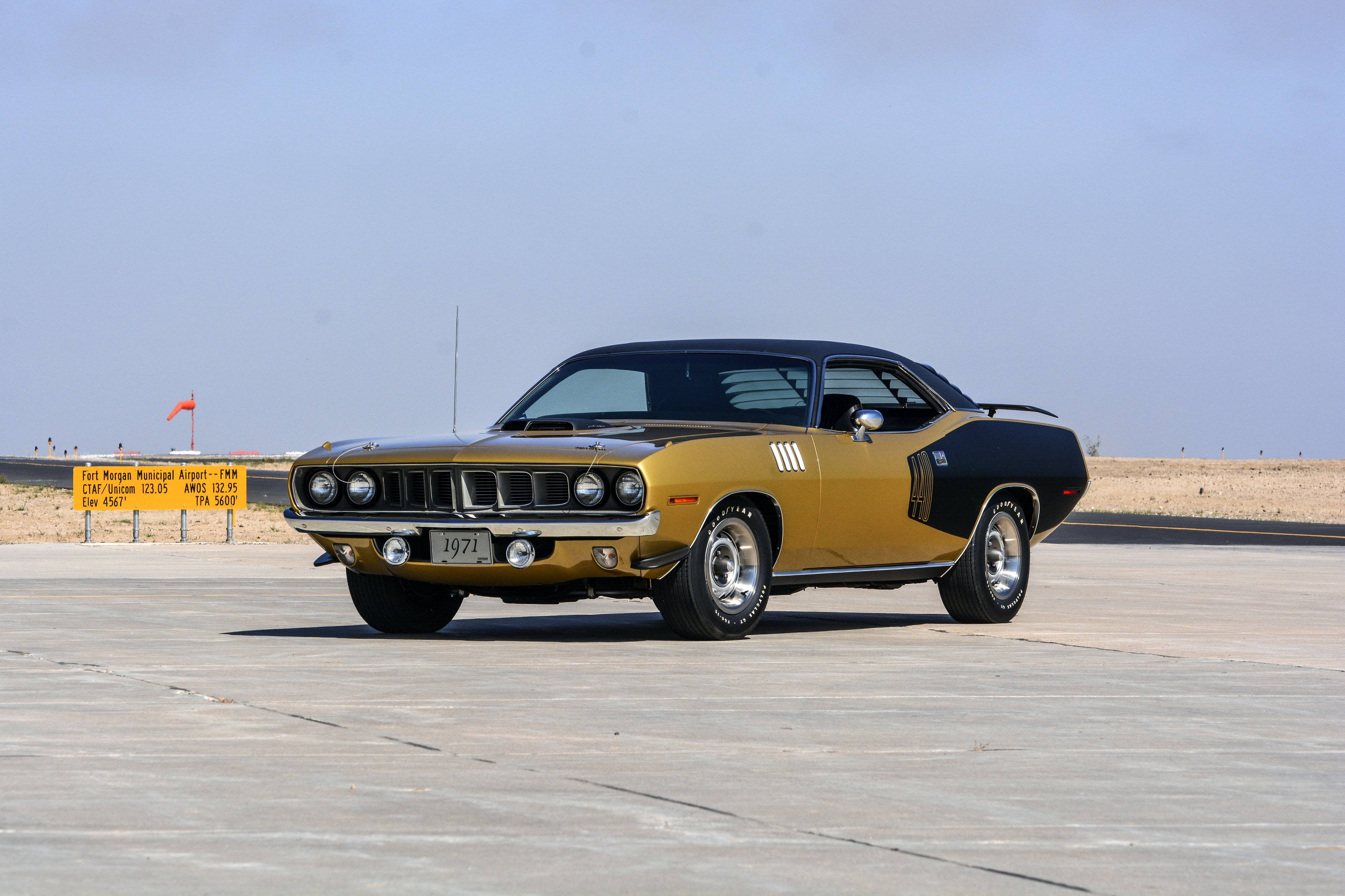 黑金1970年普利茅斯暴龍 壁紙 — 一輛金色和黑色的1971年Plymouth肌肉車停在沙漠停機坪上，天空湛藍清澈。