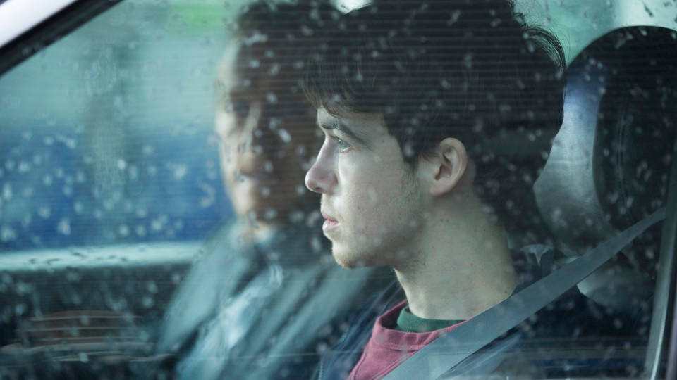 車內年輕男子望向帶雨痕的車窗，旁邊有乘客