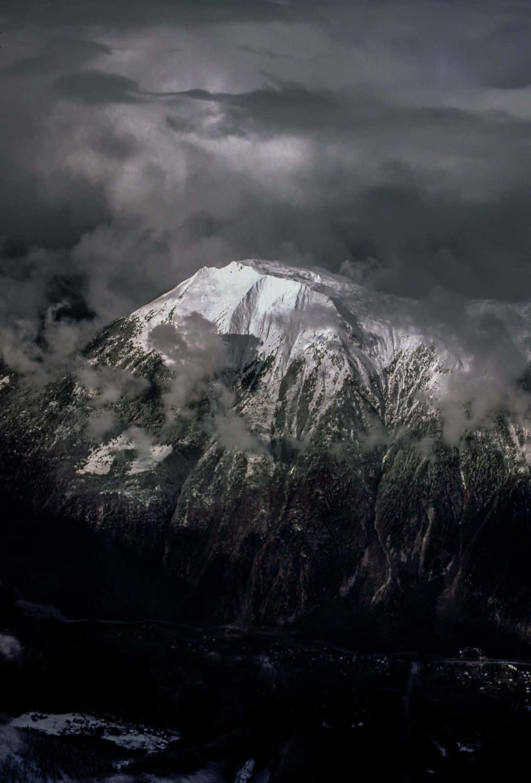 白雪覆蓋的山峰穿過黑暗的暴風雲升起，下方霧氣盤旋。