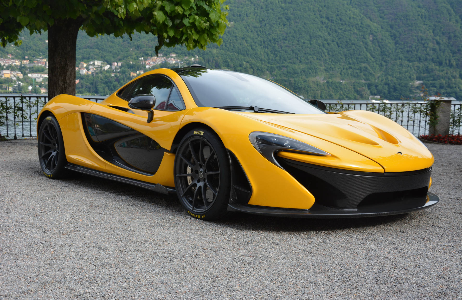 黃色McLaren P1超級跑車停在碎石路上，靠近湖泊，背景有山脈。
