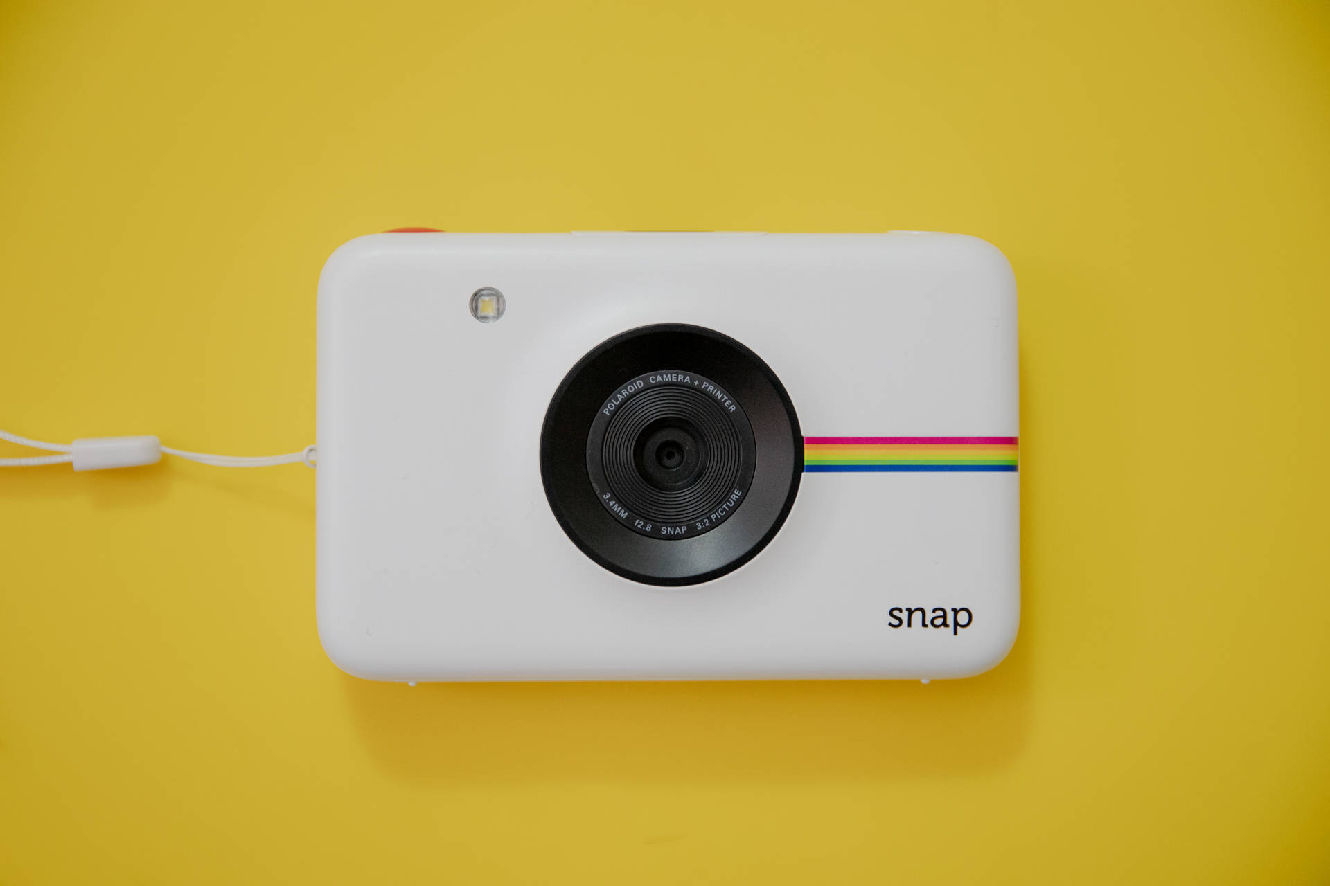 白色Polaroid Snap相機帶彩虹條紋，黃色背景。