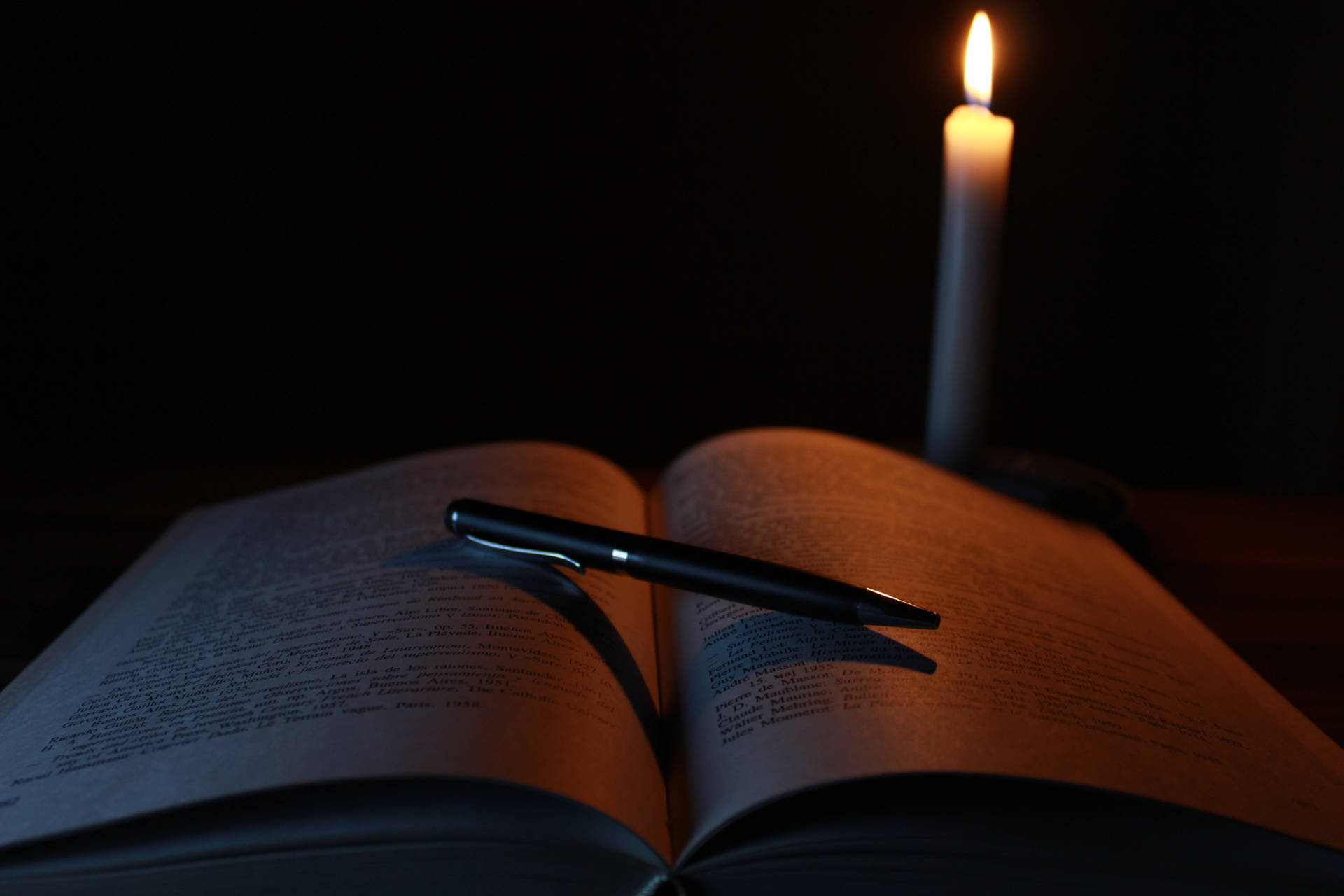 燭光照亮了一本打開的書和擱在書頁上的筆。