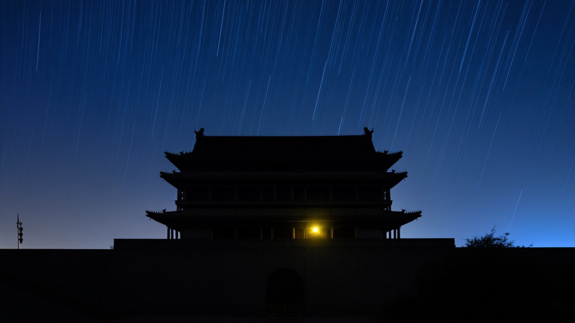 夜間星軌下古老門樓的剪影，有一扇發光的窗戶