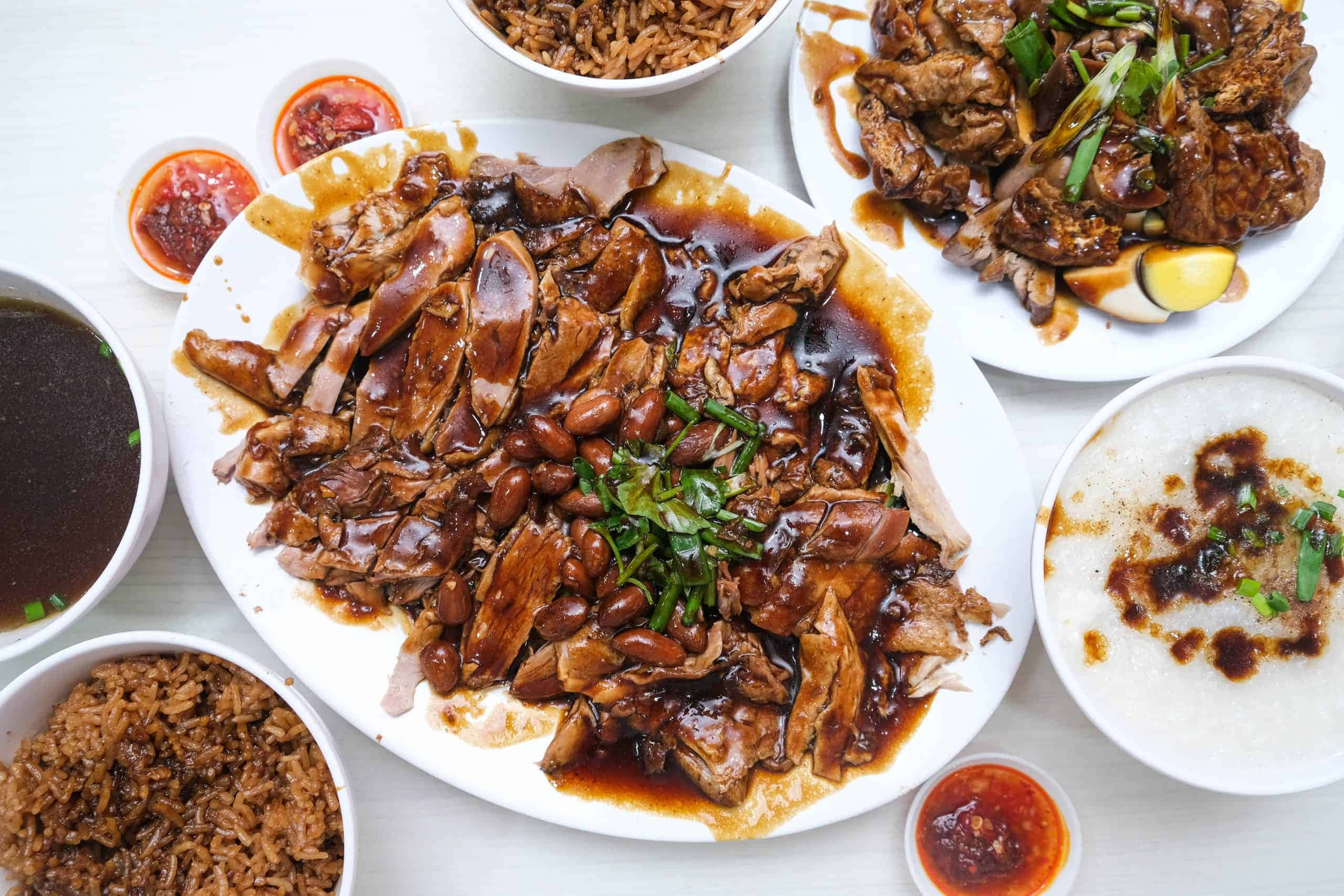 龍屋順記無骨滷鴨餐廳招牌鴨肉飯 壁紙 — 一張亮白餐桌上，擺放著豐盛的油亮烤鴨配豆類和蔬菜，周圍環繞著飯碗和蘸醬。