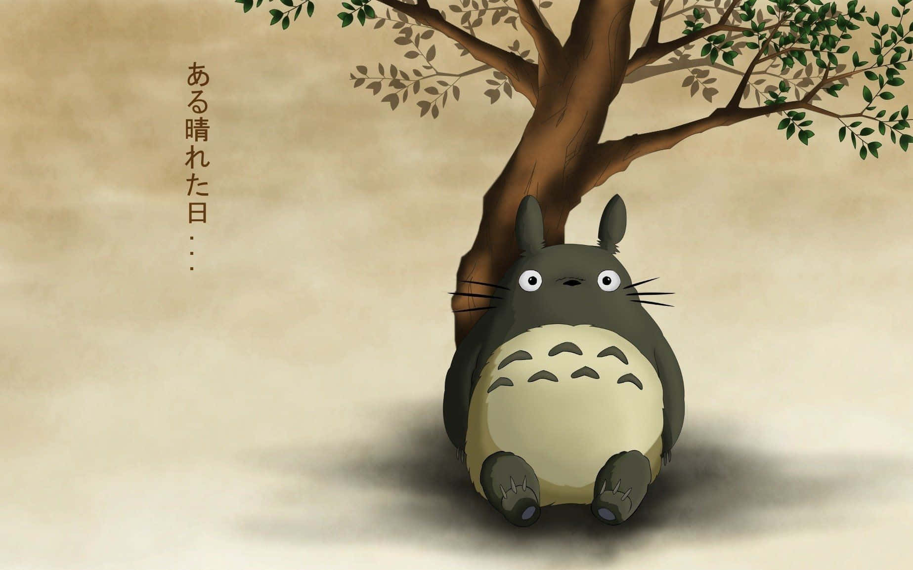 一個灰色龍貓角色坐在一棵有綠葉的樹下。