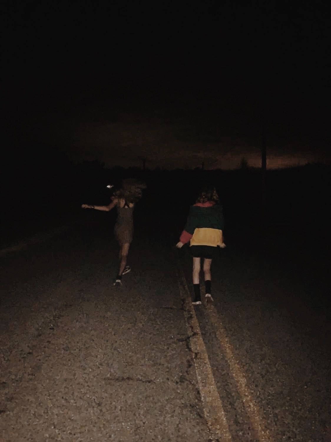 兩個人在夜晚的黑暗道路上走遠，地平線上有橙色光芒。