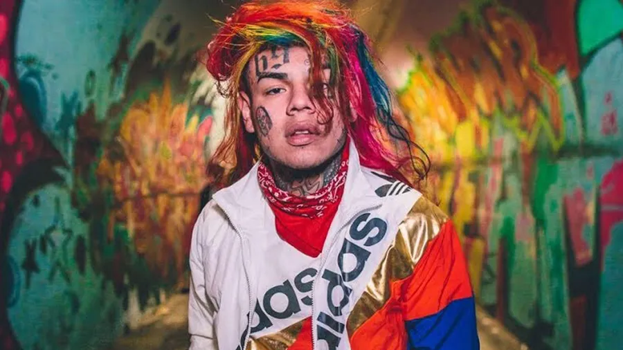 擁有彩虹頭髮和紋身的人站在塗鴉牆前穿著Adidas外套。
