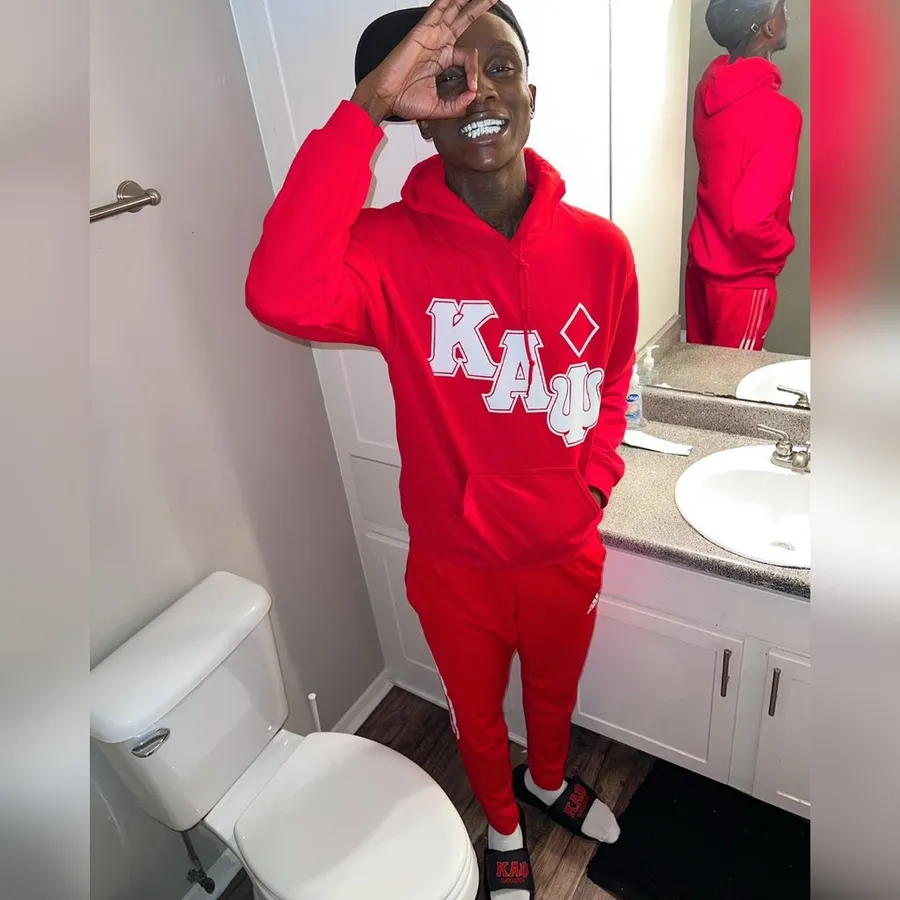 身穿紅色Kappa運動服的男人在浴室鏡中微笑並做手勢。