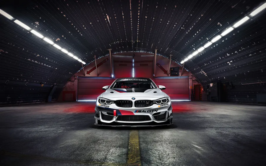 白色BMW M4 GT4賽車在黑暗的工業車庫中,頂燈明亮。