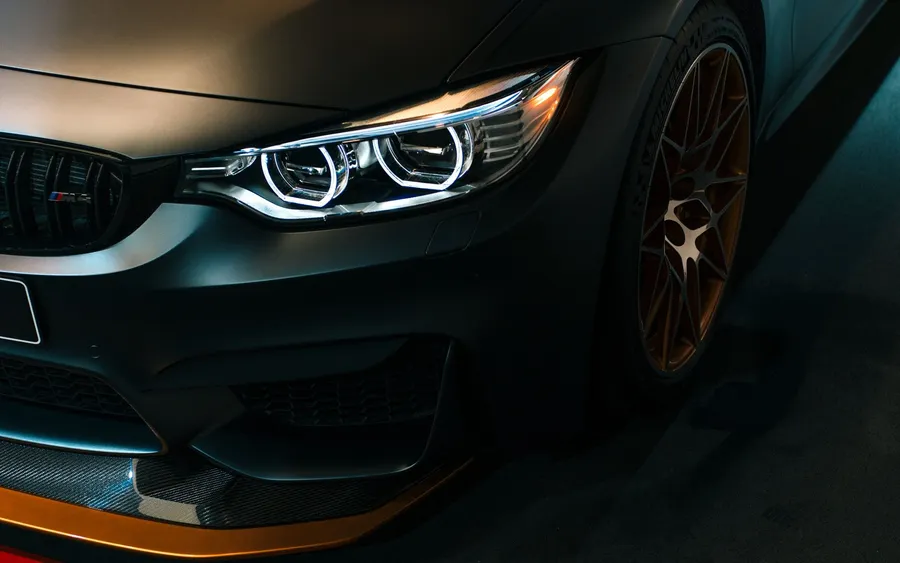 啞光黑色BMW M4,配金色輪圈和照明頭燈,在黑暗的工作室環境中。