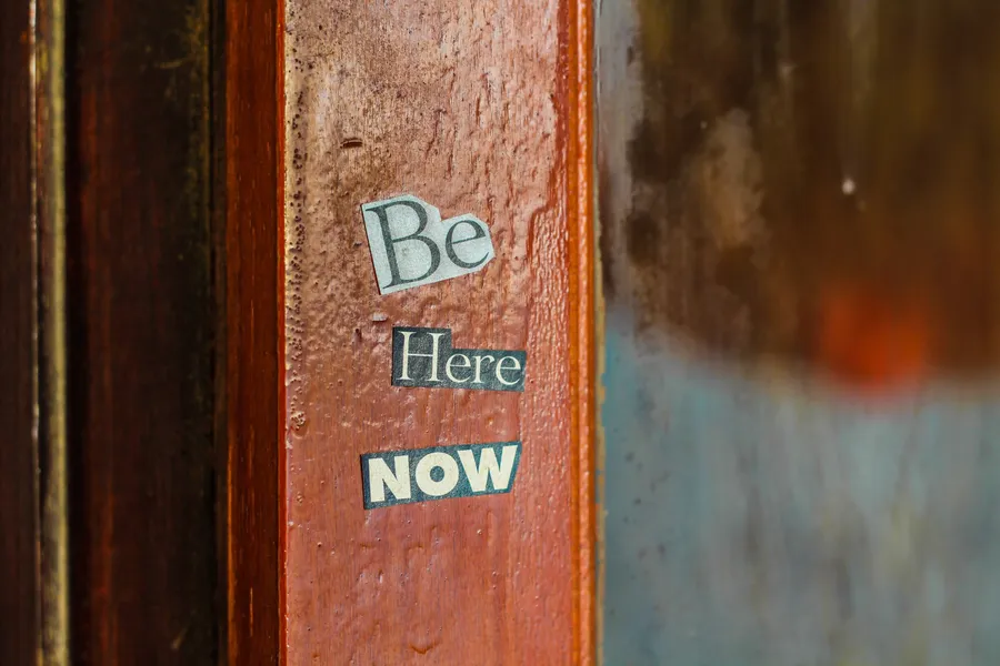 寫有 'Be Here Now' 的勵志貼紙,貼在質樸的木門框上。