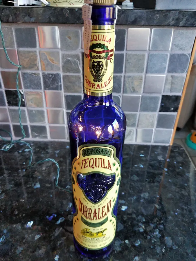 花崗岩檯面上的藍色龍舌蘭酒瓶,後面有馬賽克瓷磚牆。