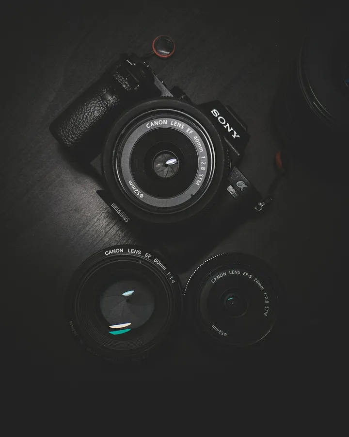 深色木質表面上排列的Sony相機和Canon鏡頭。