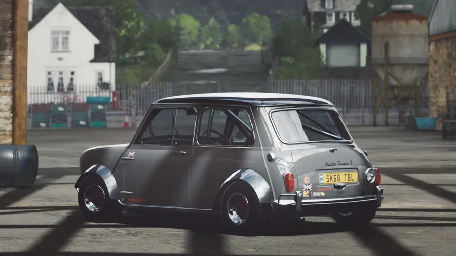 銀色經典Mini Cooper S賽車在工業庭院中,背景有石建築物和綠色植物。