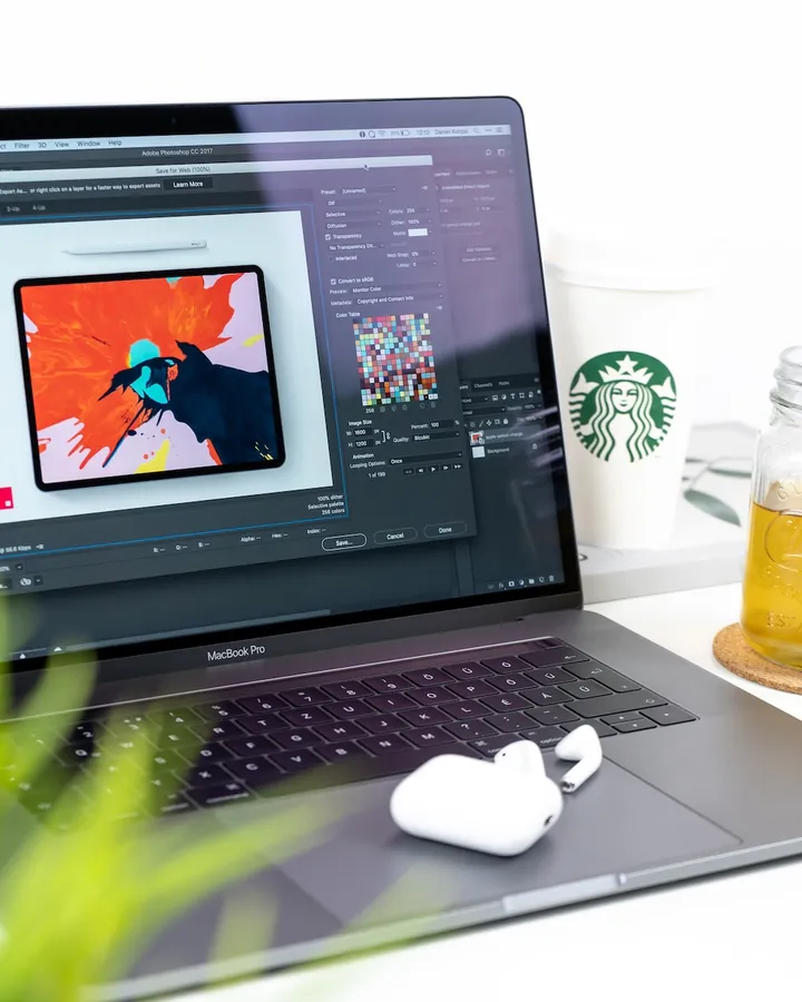 MacBook Pro 打開數位藝術,旁邊放著咖啡和耳塞,在乾淨的桌子上。