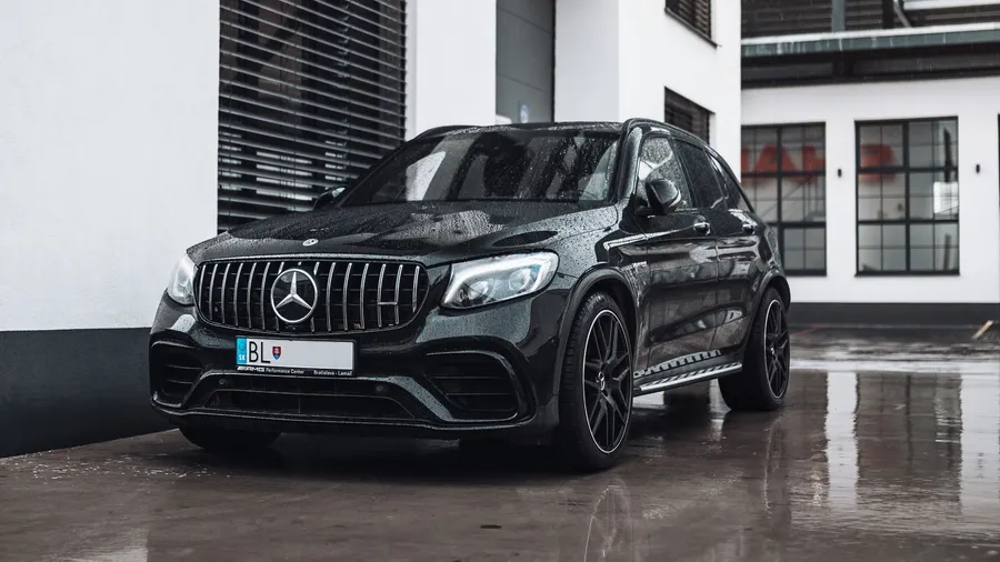 黑色Mercedes-AMG GLC 63 S SUV停在濕路面上,帶有建築物倒影。
