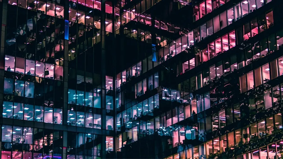 現代辦公樓的夜景,明亮的窗戶顯示內部的工人。